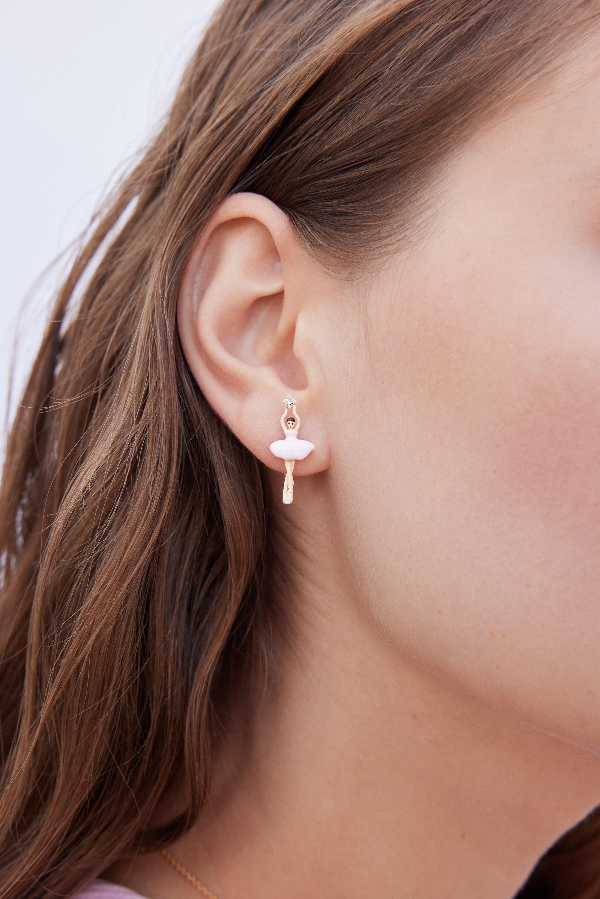 Single gold-toned ballerina earring with light pink tutu, skin-toned body, and a clear gem held above her head.