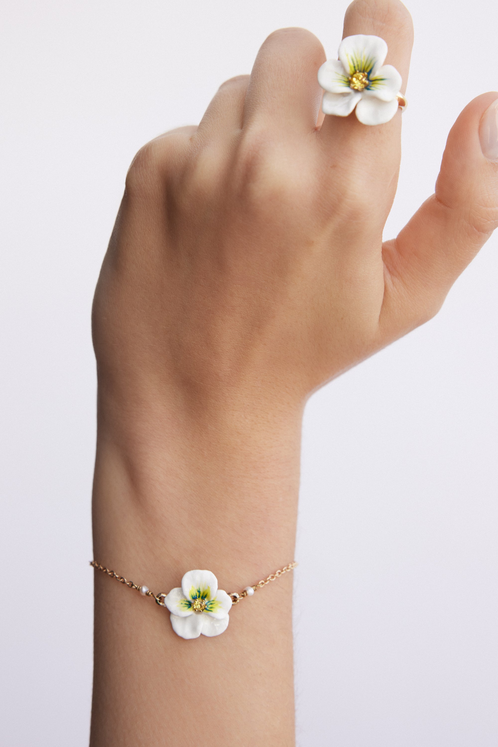 Gold-toned chain bracelet with a white flower charm featuring green accents and a yellow center, flanked by small white beads