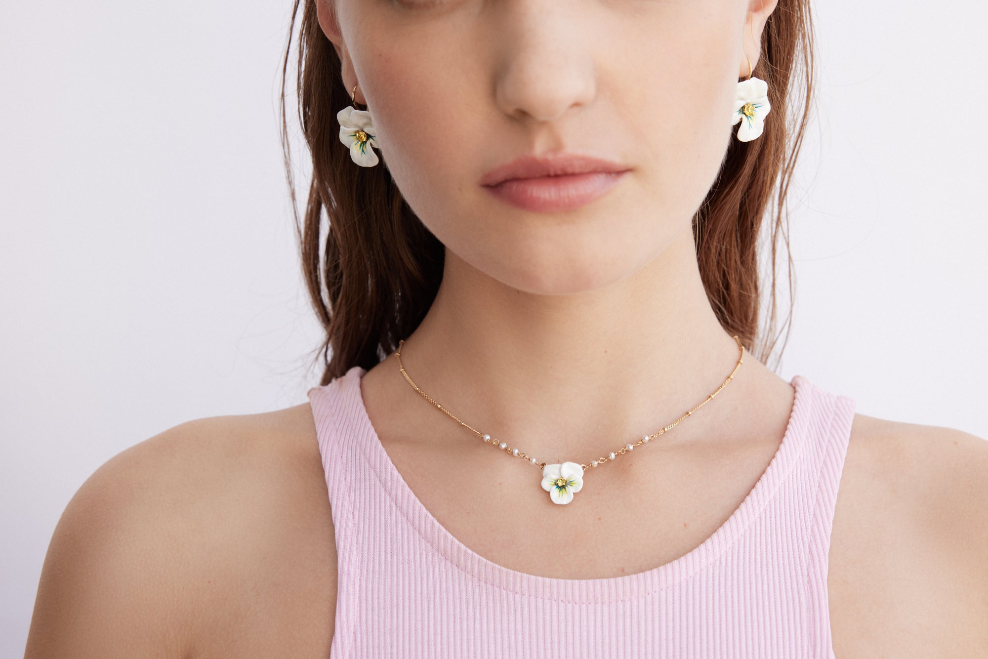 Gold-toned necklace with a delicate chain, small white pearls, and a white pansy flower pendant with a green and yellow cente