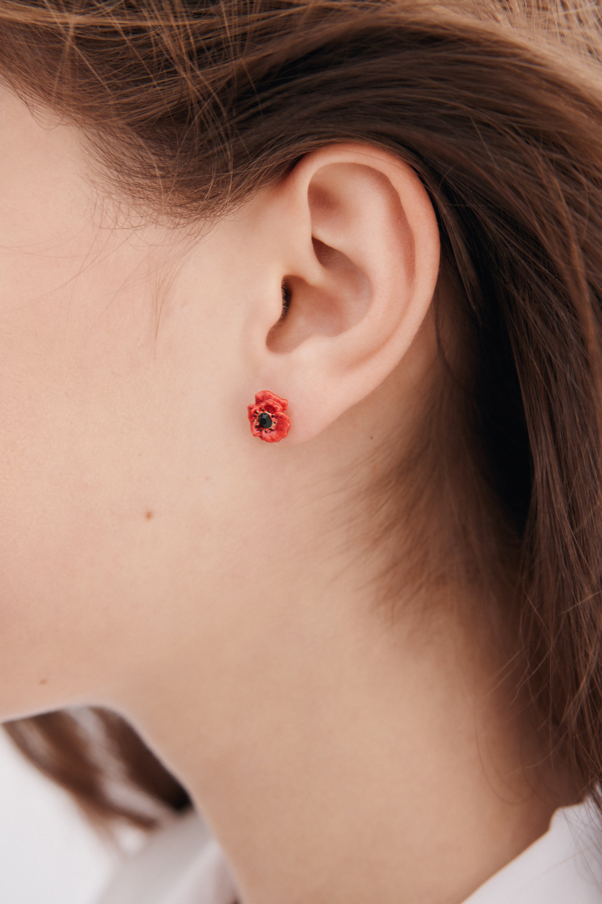 A single stud earring shaped like a poppy flower with reddish-orange petals and a black center.