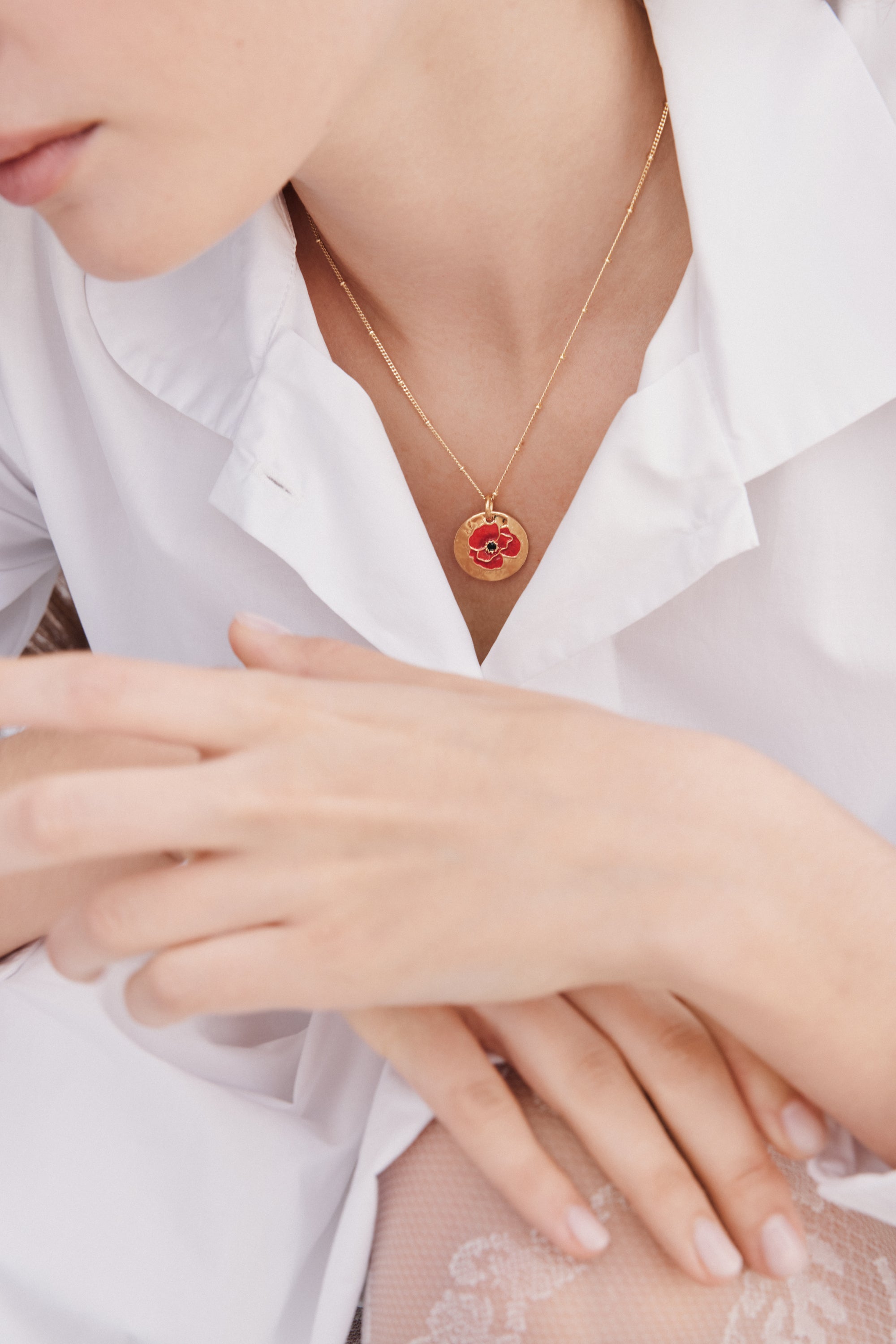 Gold-toned beaded chain necklace with a circular gold-toned pendant featuring a red poppy flower with black details.