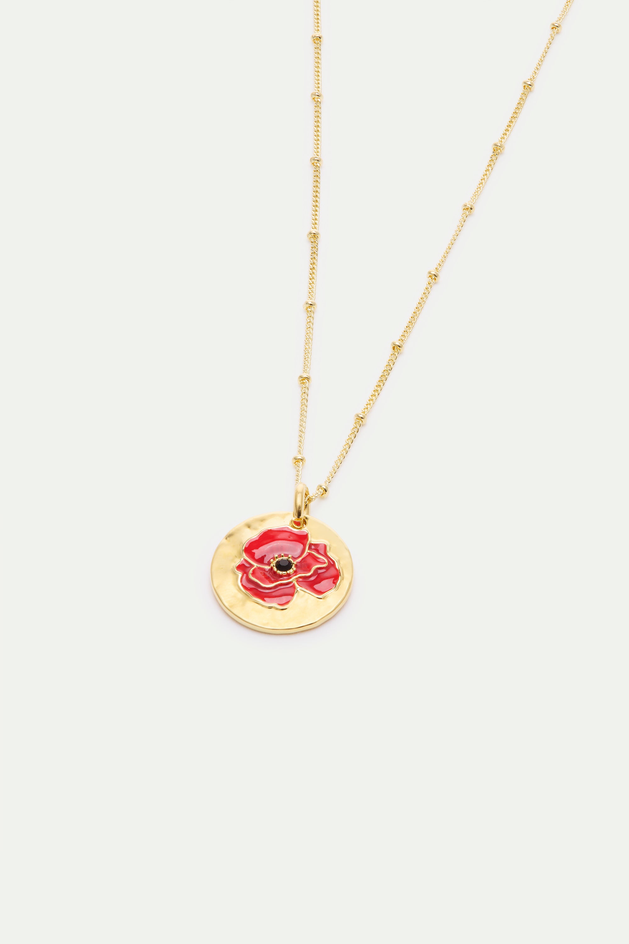 Gold-toned necklace with a beaded chain and a hammered circular pendant featuring a red poppy with a black center.