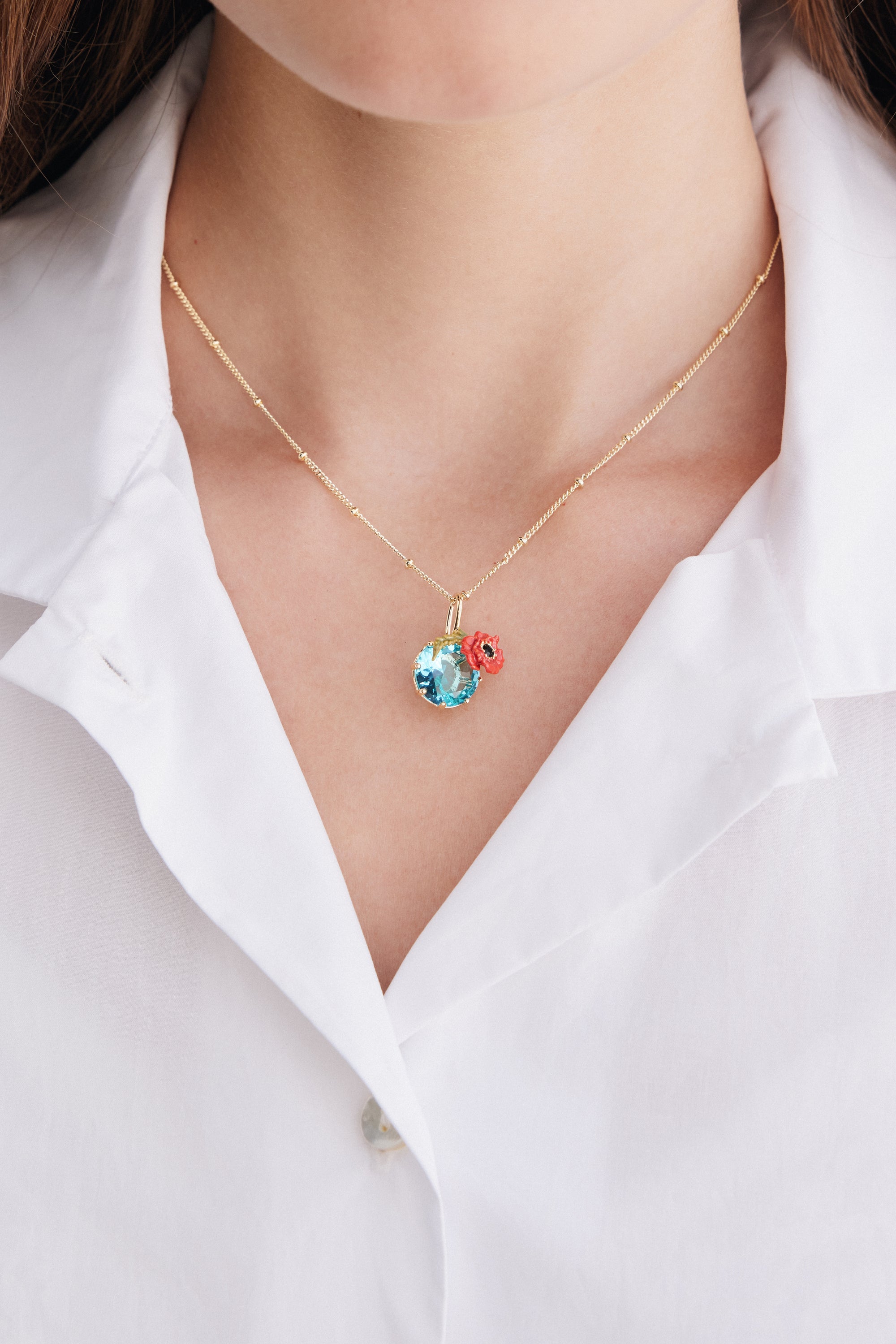 Gold-toned beaded chain necklace with a large faceted light blue stone pendant and a small red poppy flower detail.