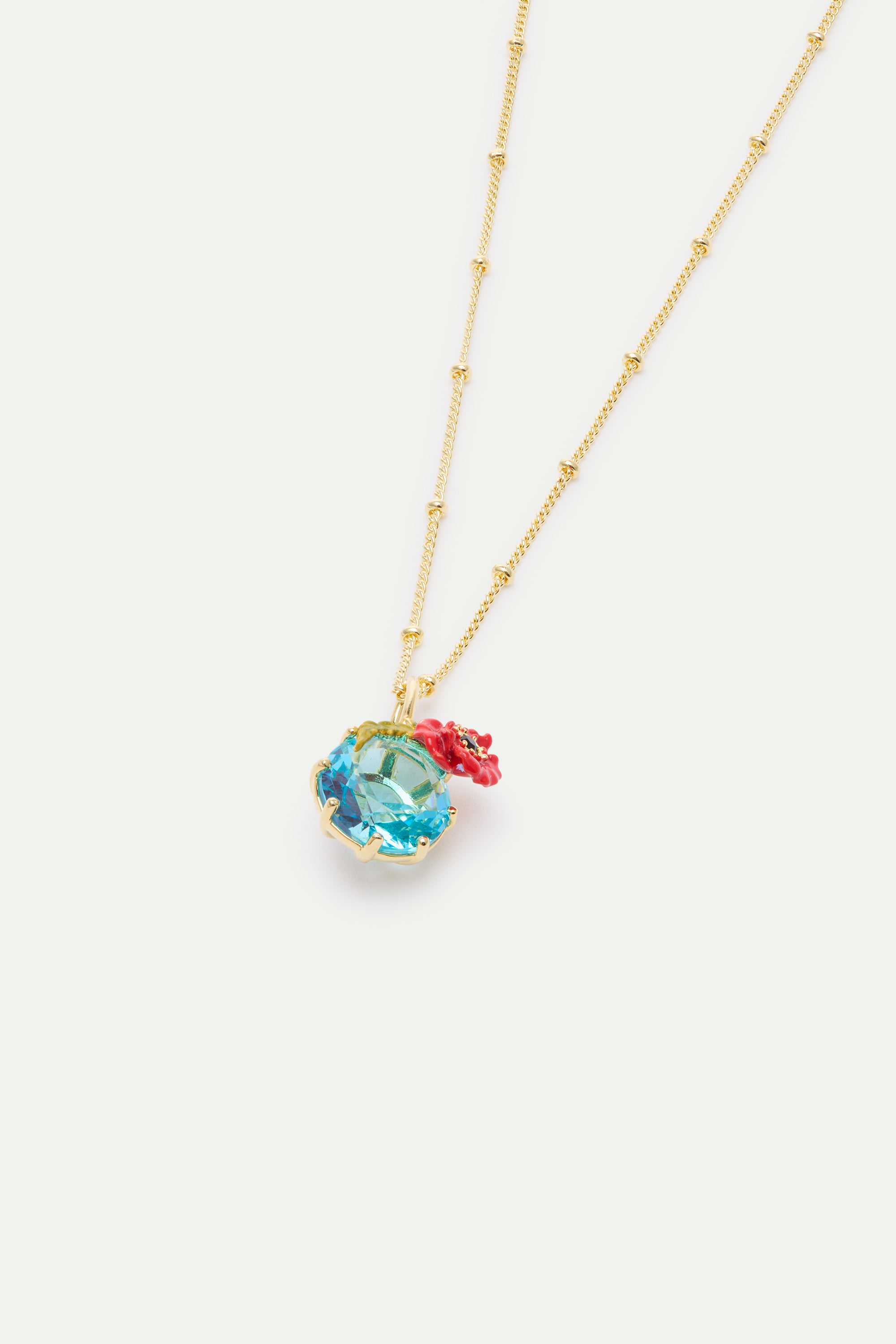 Gold-toned beaded chain necklace with a faceted light blue stone pendant, accented by a small red poppy flower and green leav