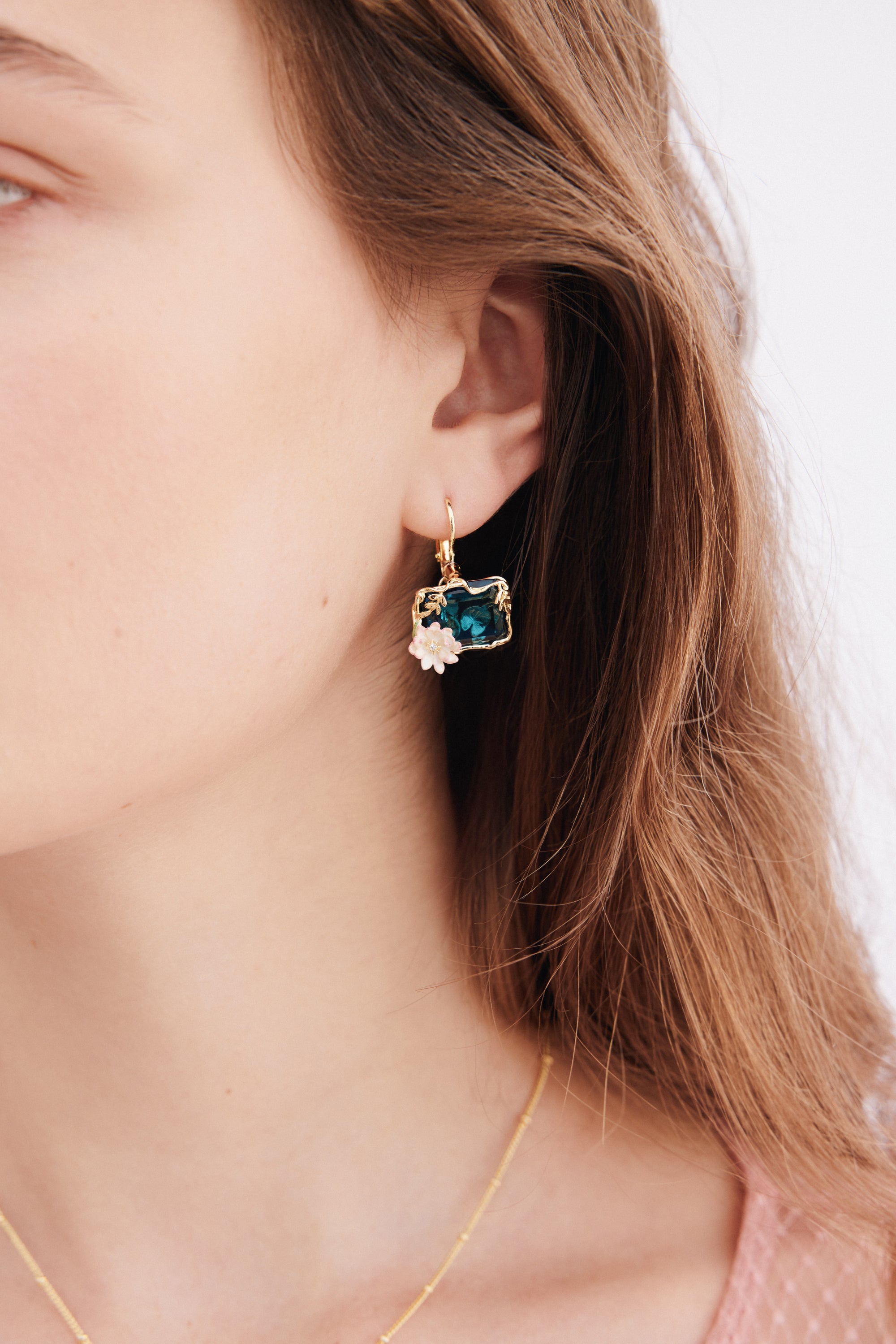 A single gold-toned sleeper earring with a rectangular dark teal gem in an ornate gold-toned frame, accented by two small lig