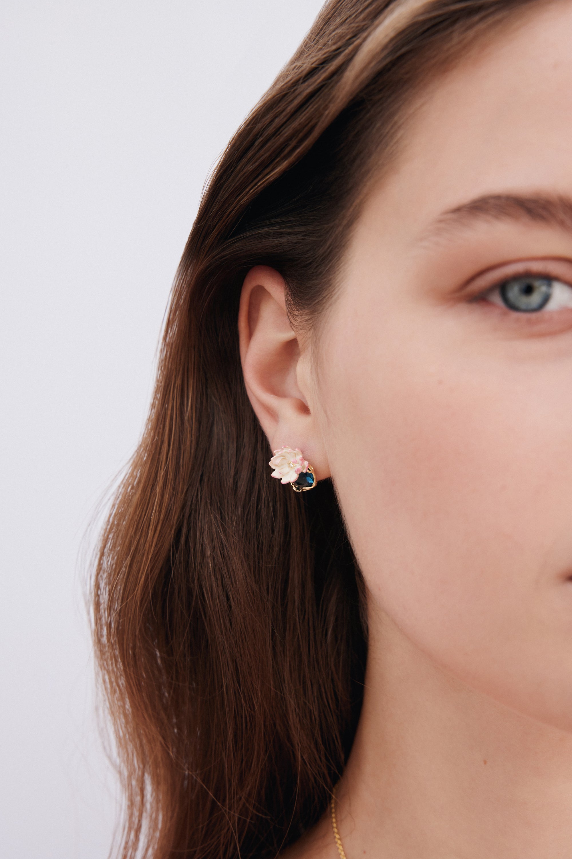 A single post earring with a light pink and white flower design, featuring a dark blue stone in a gold-toned setting.