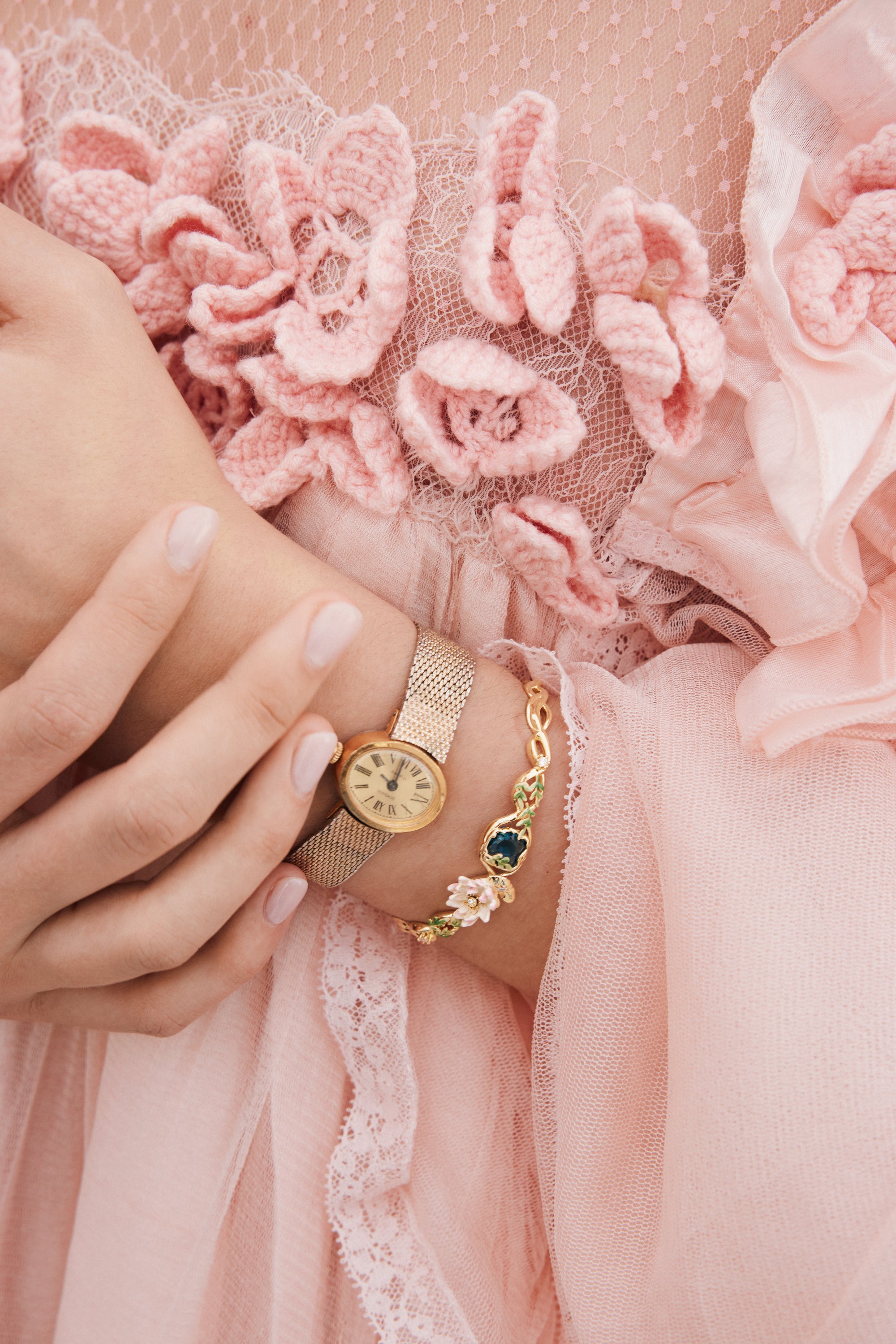 Gold-toned cuff bracelet with a floral design featuring light pink flowers, green leaves, and a central dark blue oval stone.