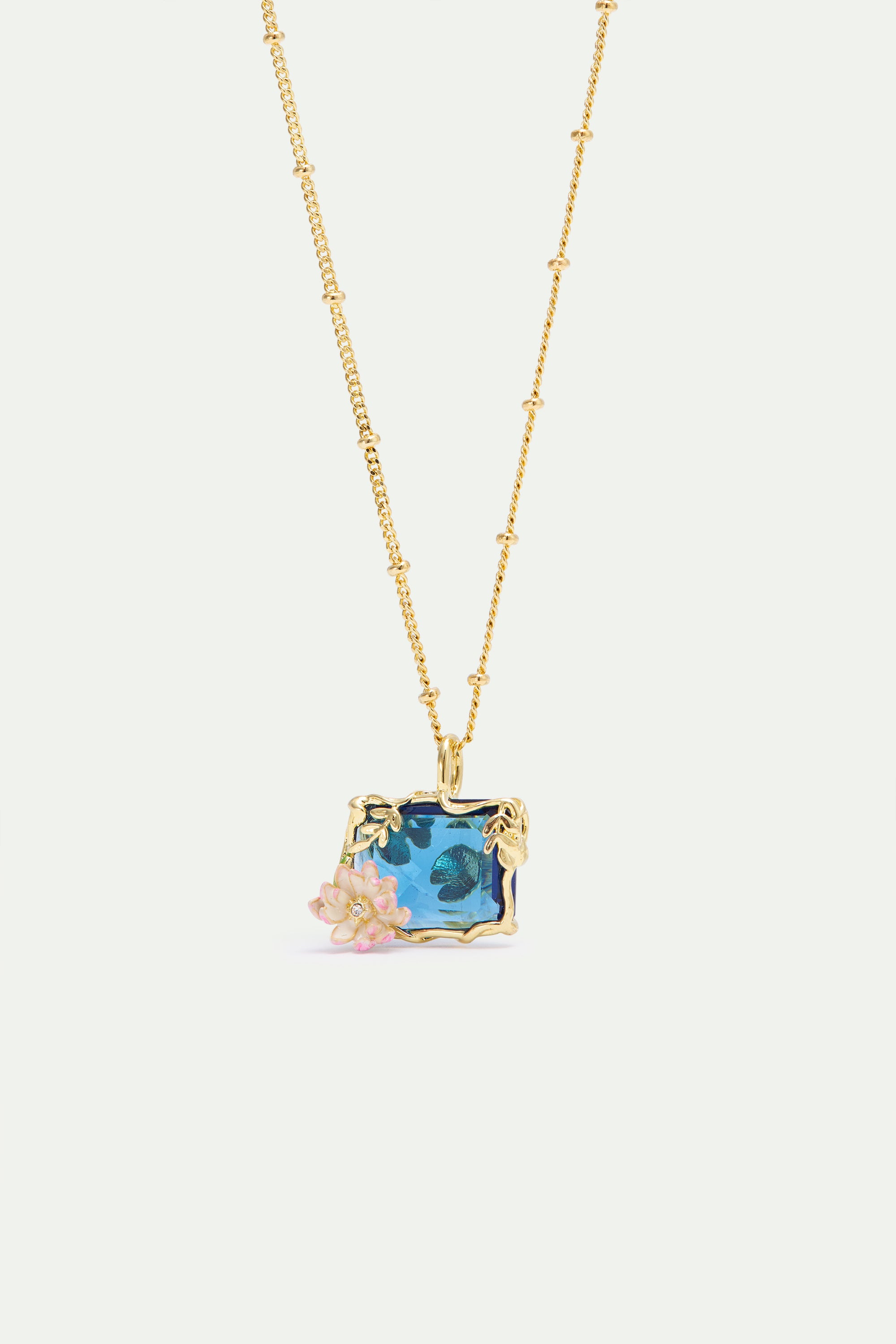 Gold-toned necklace with a rectangular blue faceted pendant featuring a water lily design and pink sculpted flowers.