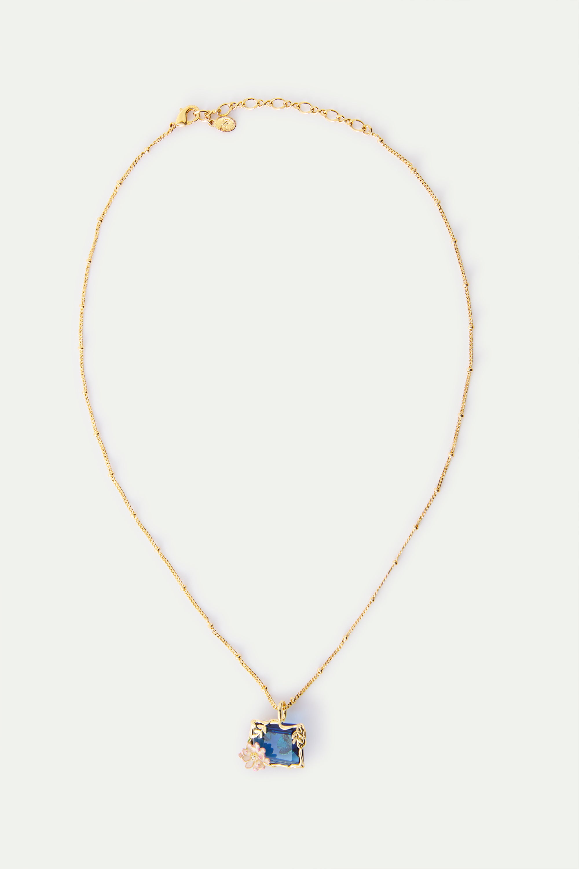 Gold-toned necklace with a delicate beaded chain. Features a rectangular deep blue pendant framed in gold-toned metal with a