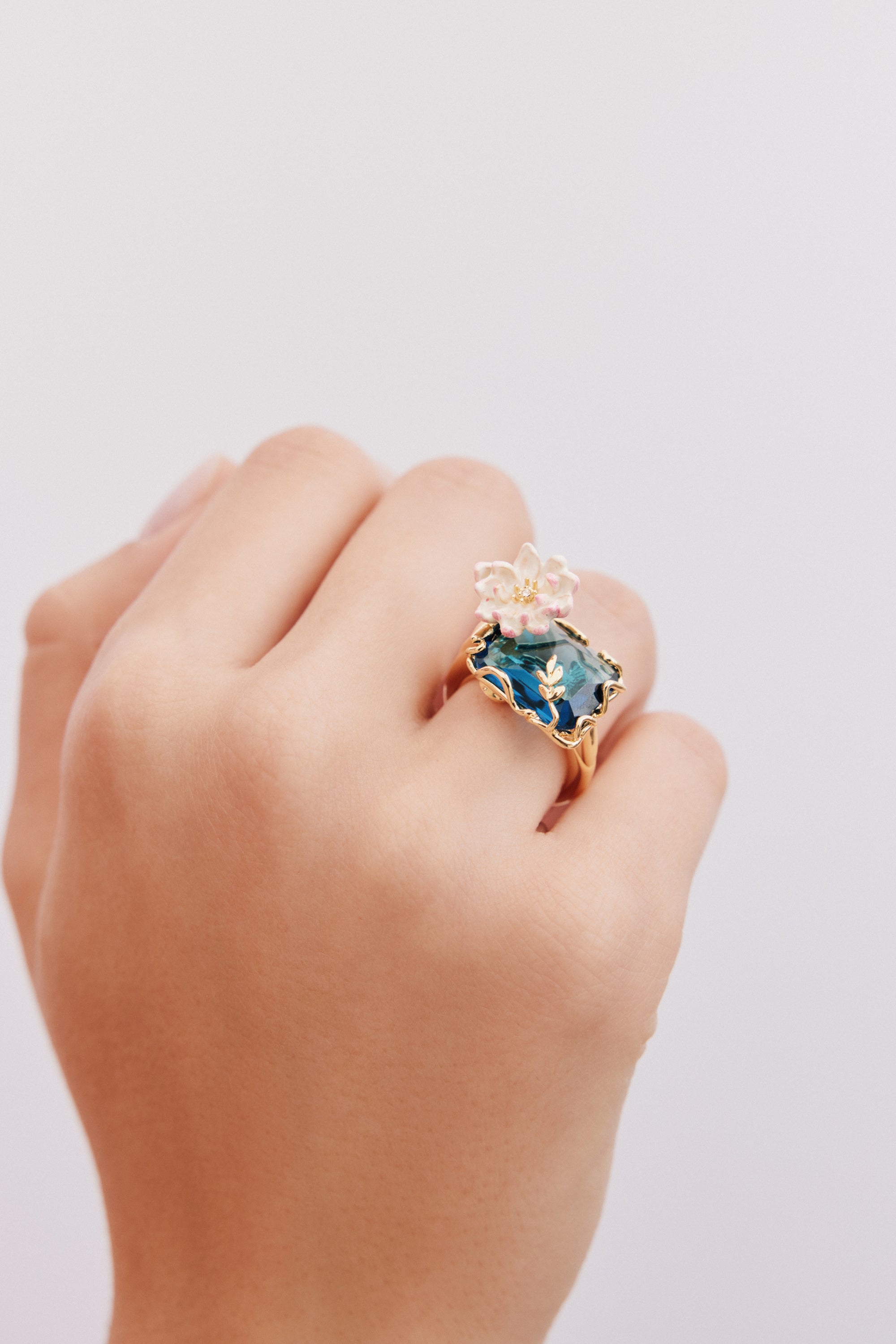 Gold-toned ring with a large blue-green rectangular stone, featuring gold-toned leaf details with blue enamel and a white/pin