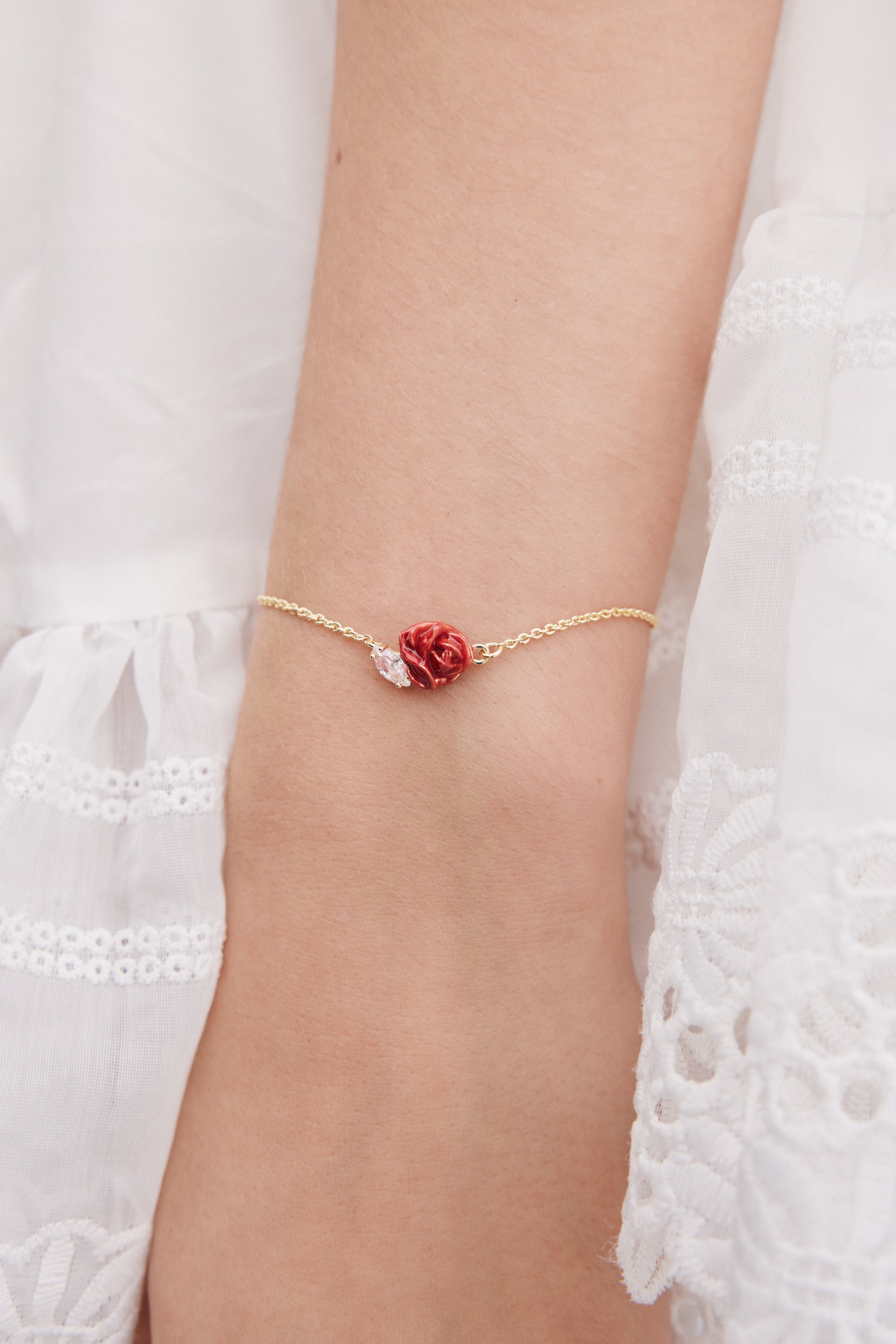 Delicate gold-toned chain bracelet with a small red rose charm and a clear marquise-cut stone.