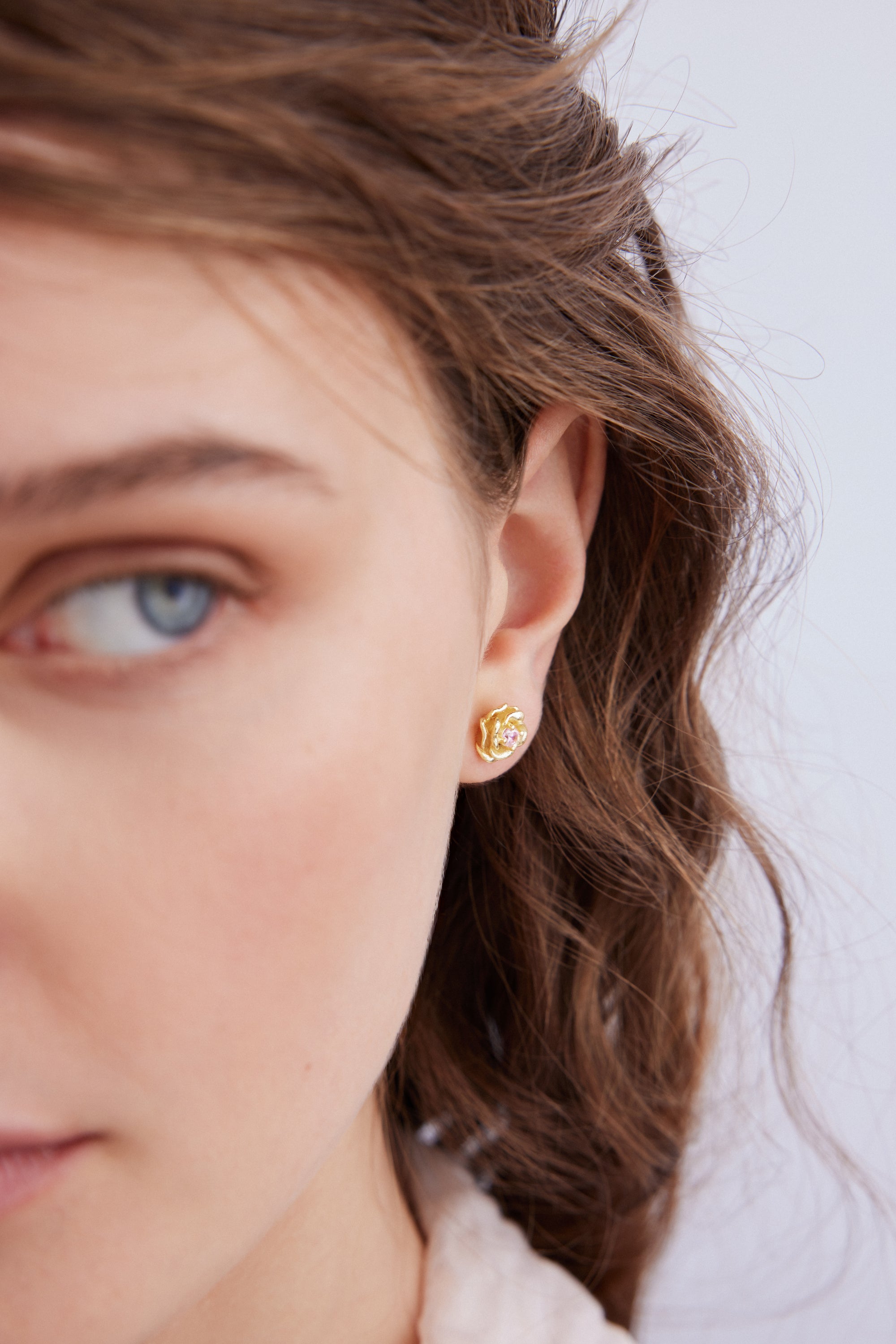 Gold-toned rose stud earring with a small light pink stone in the center.