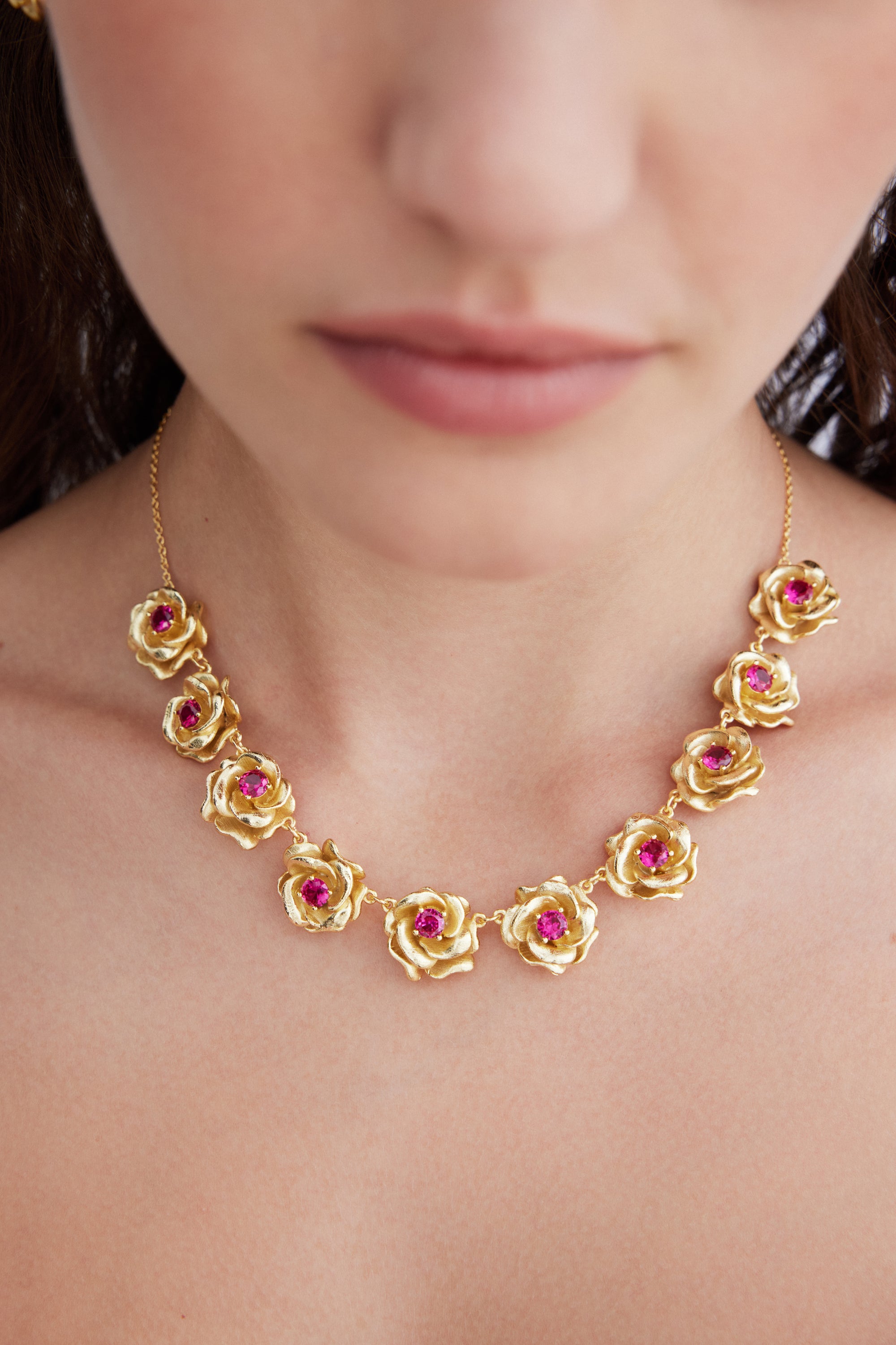 Gold-toned necklace with a delicate chain and eleven linked rose-shaped elements, each centered with a fuchsia stone.