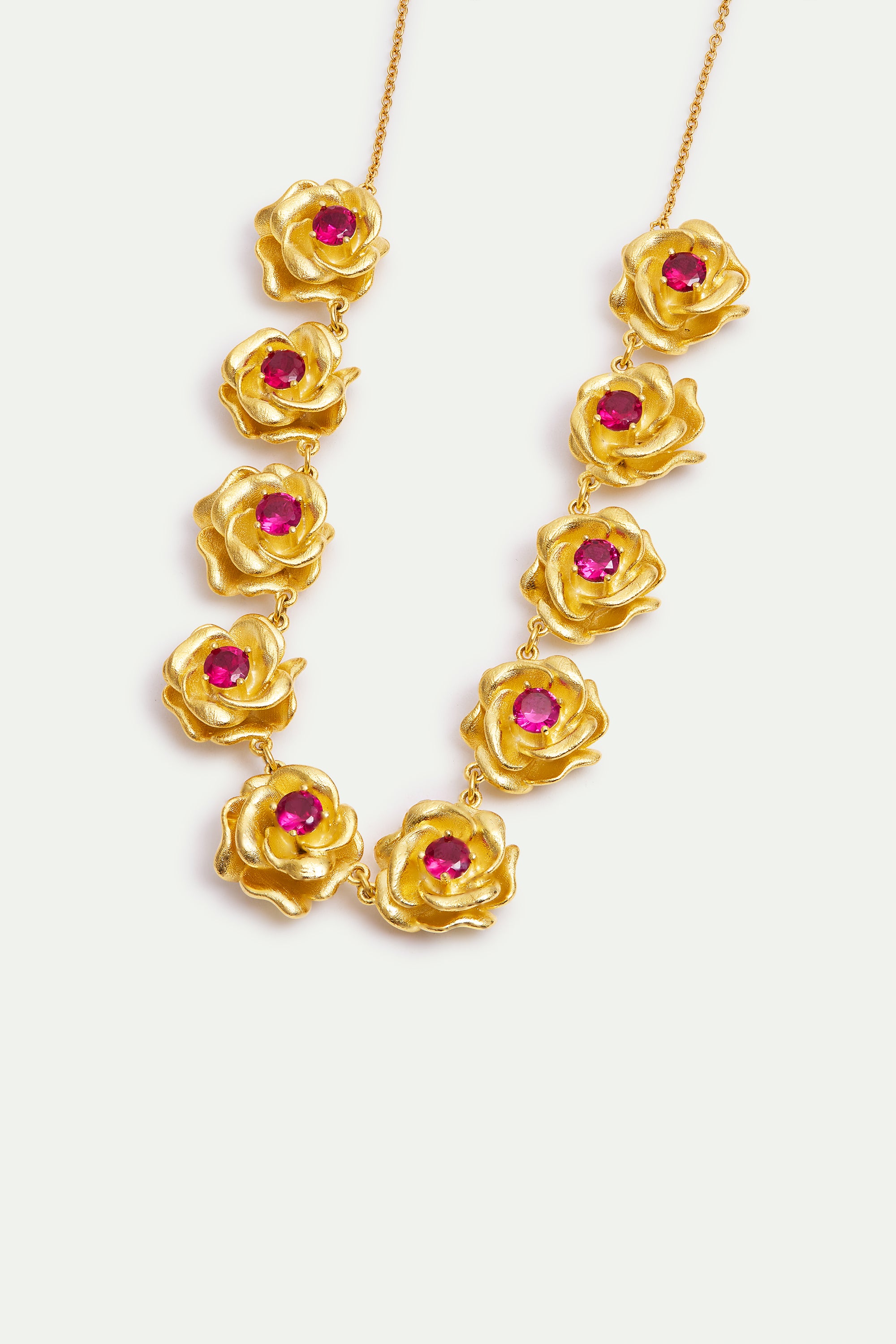 Gold-toned necklace with 10 rose-shaped links, each featuring a fuchsia gemstone in its center.