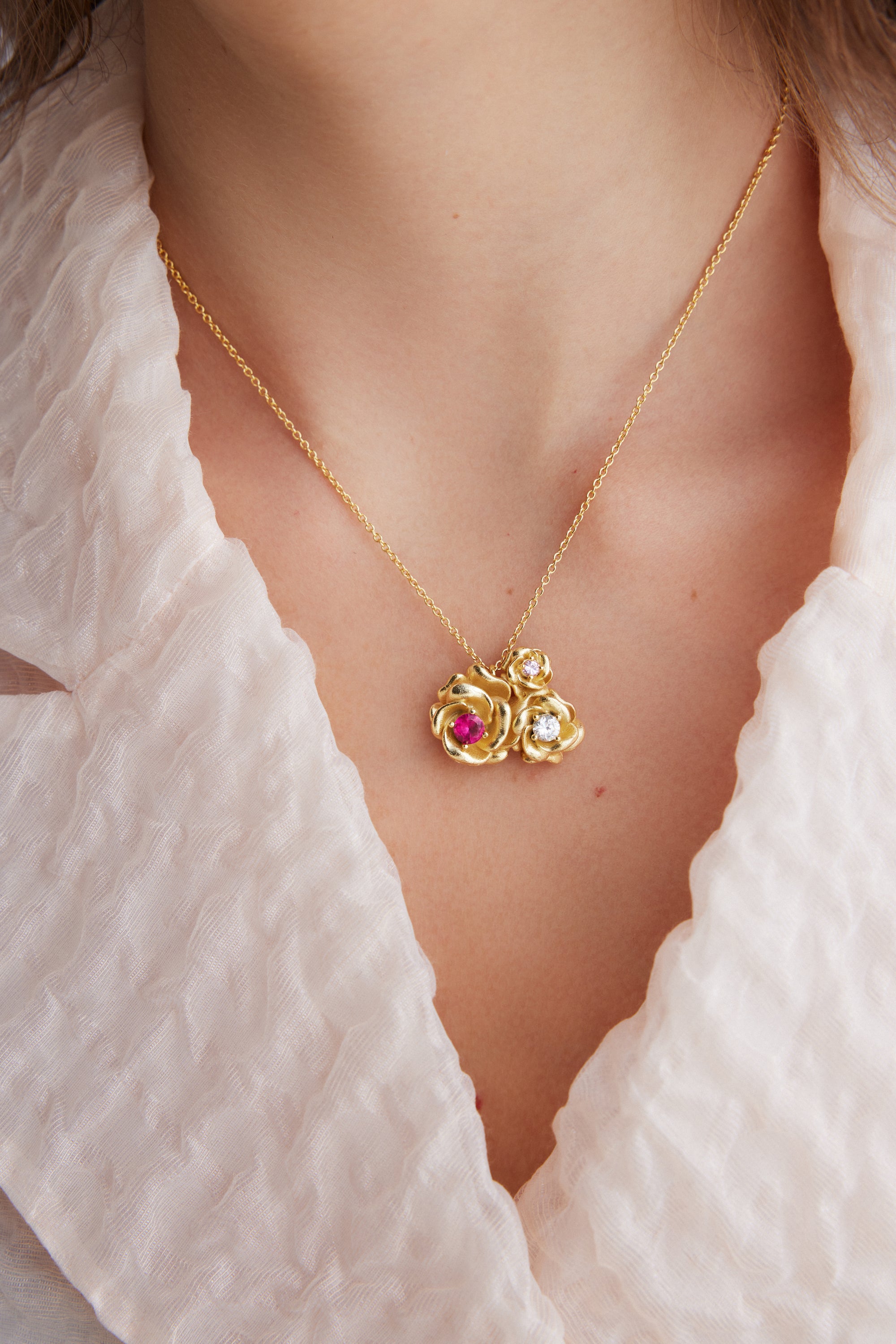 Gold-toned necklace with a pendant of three rose-shaped elements. One large rose has a red stone, and two smaller roses have