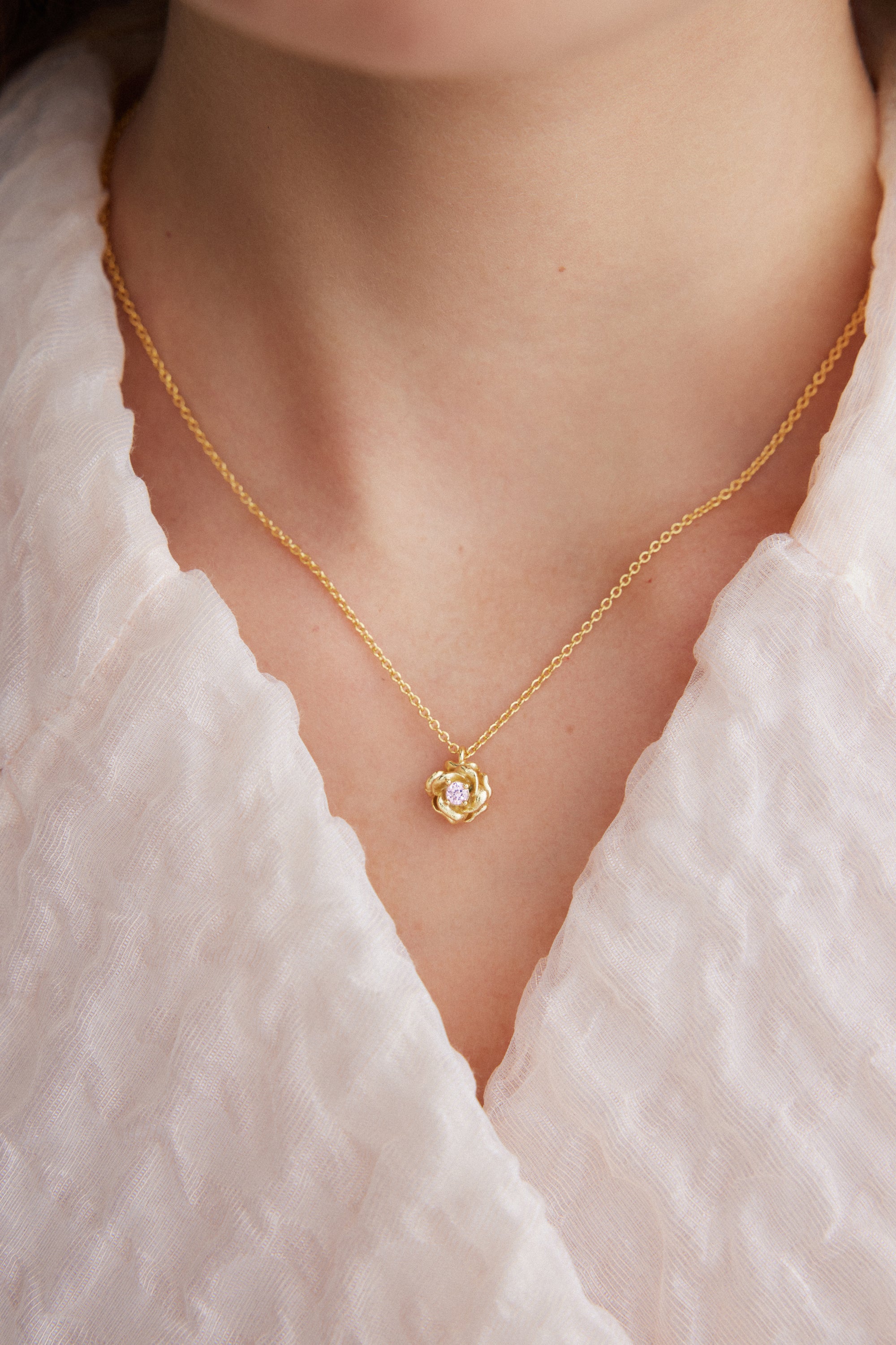 Gold-toned necklace with a delicate chain and a small rosebud pendant featuring a clear round stone in its center.