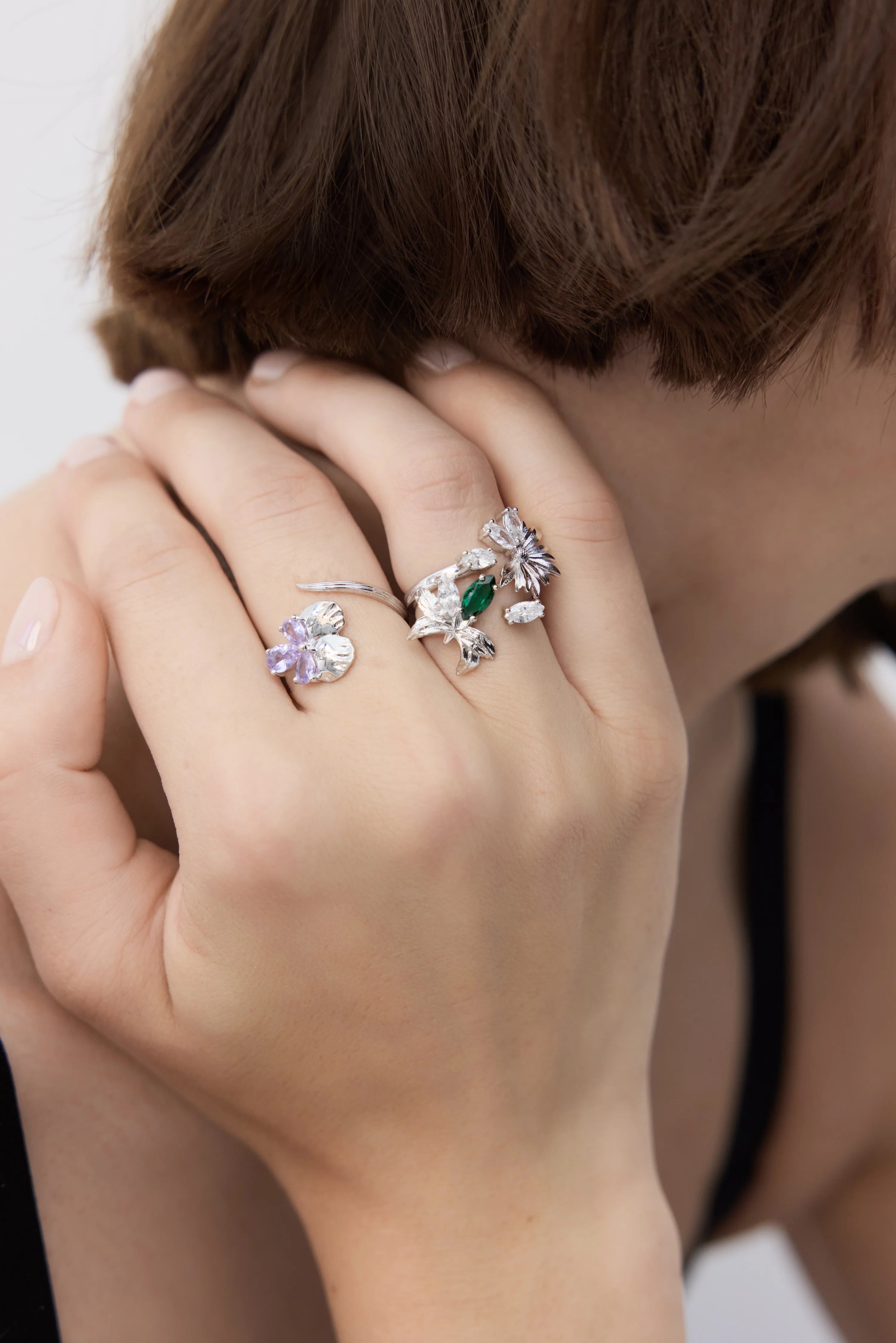 Adjustable silver-toned ring with a textured band. One end has a purple flower, the other a cluster of clear and green floral