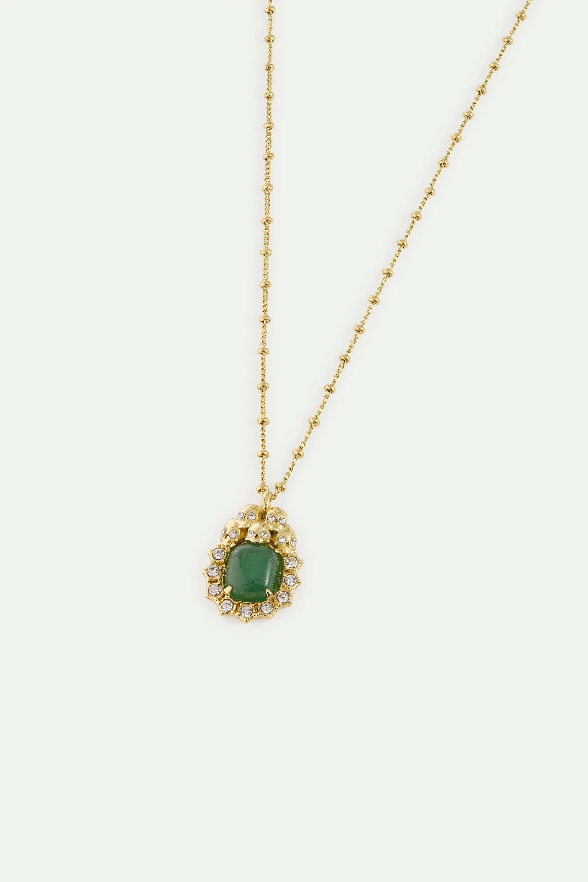 Gold-toned bead chain necklace with a green cushion-cut stone pendant surrounded by clear crystals and small skull motifs.