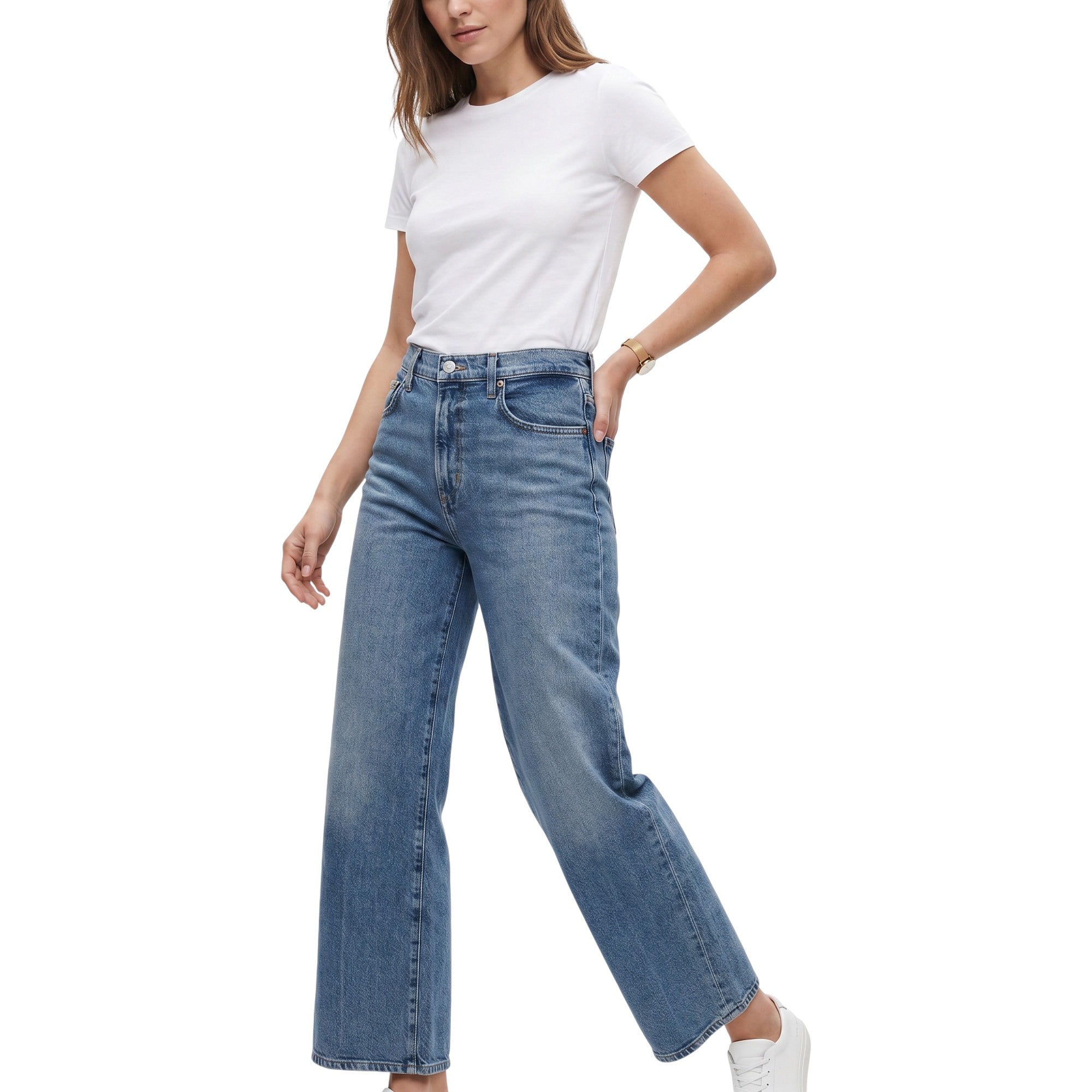 A model wearing a pair of high-waisted, wide-leg blue jeans with a white t-shirt and white sneakers, shown from the waist down against a plain white background.
