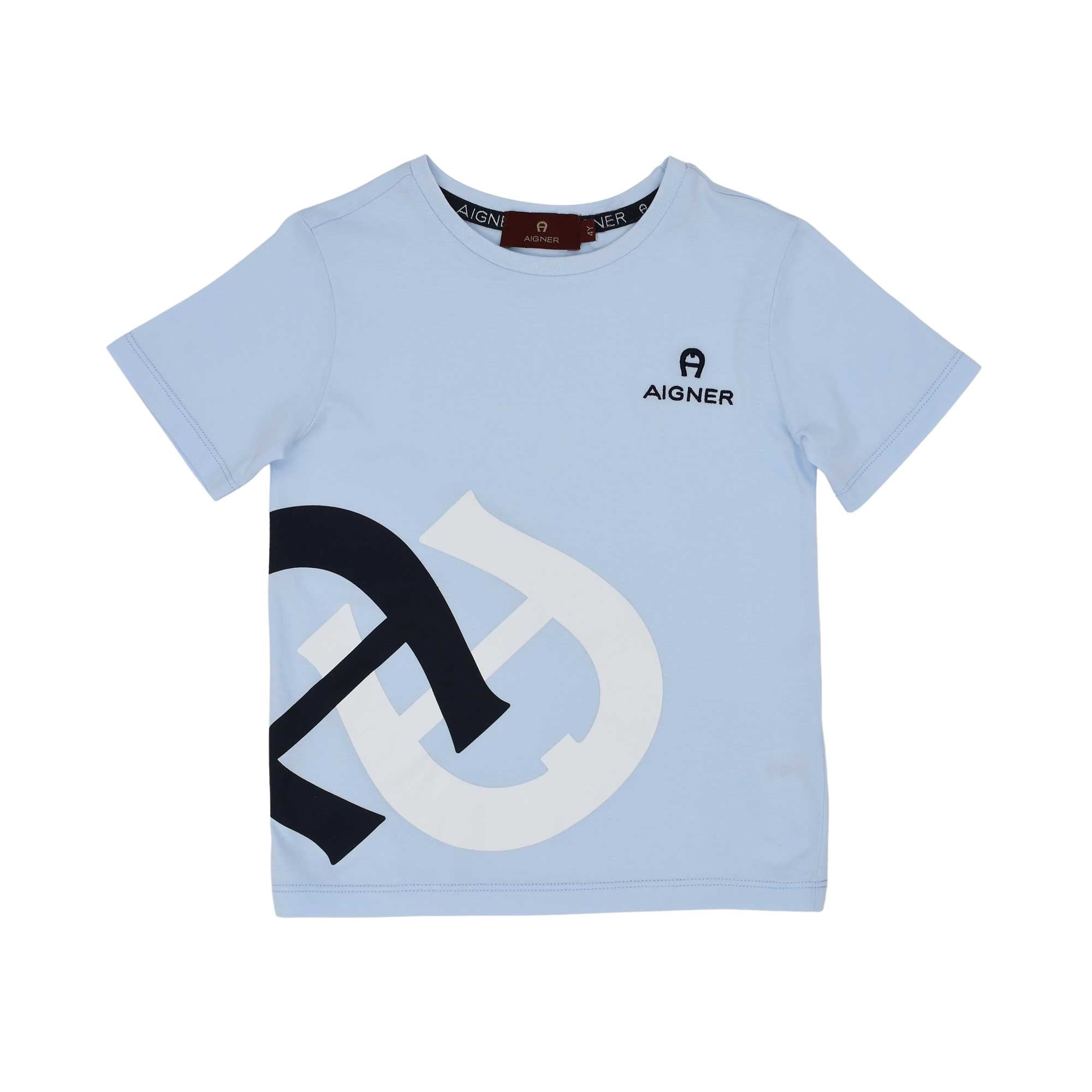 A light blue short-sleeved T-shirt for boys by Aigner Kids. The shirt features a small navy logo on the chest and a large, bold navy and white interlocking horseshoe graphic on the lower right side.