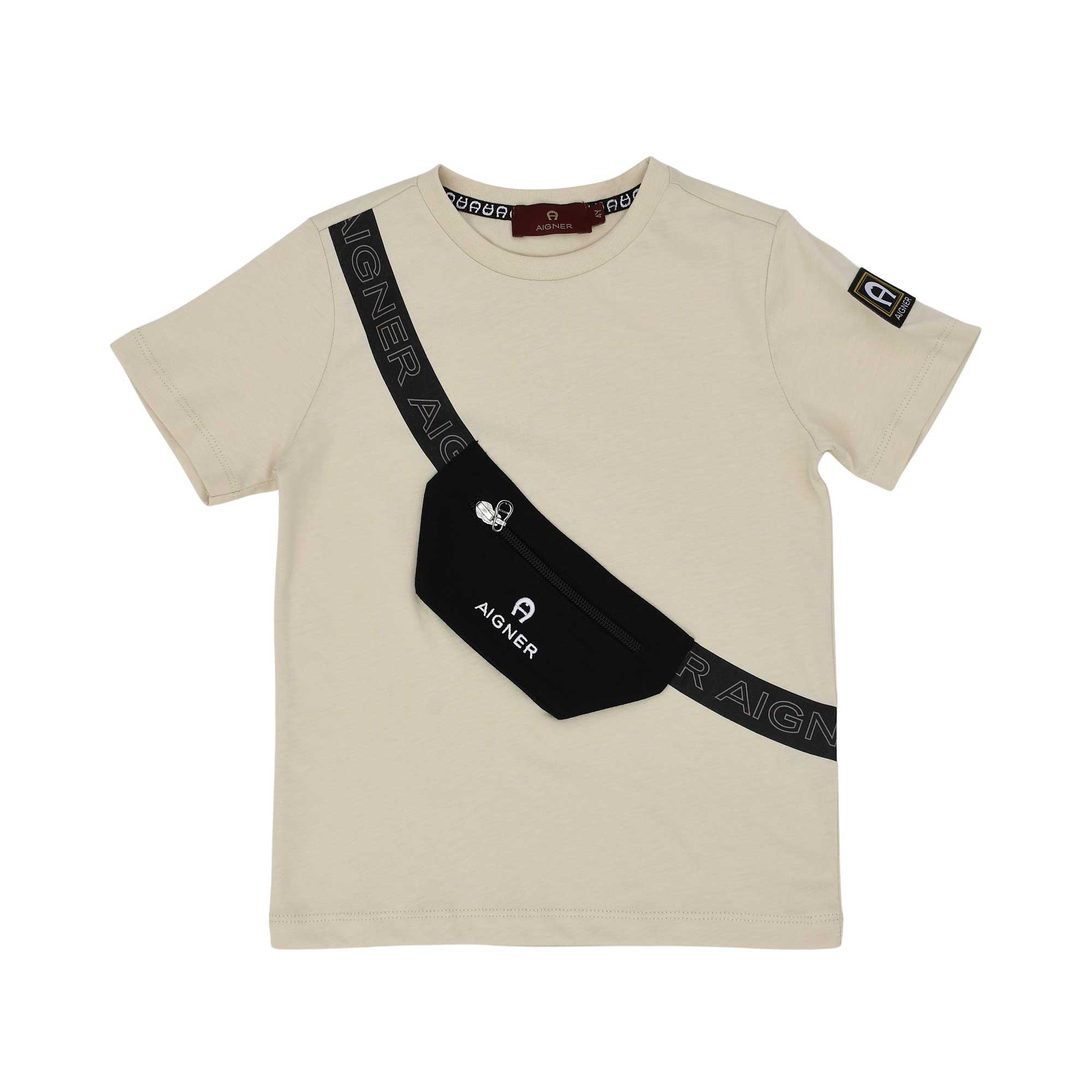 A beige boys' T-shirt by Aigner Kids featuring a diagonal black strap print and a 3D-effect black pouch with a zipper, resembling a crossbody bag. A small logo patch is visible on the left sleeve.