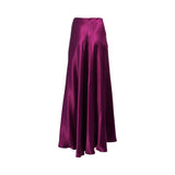 Front three-quarter view of a luxurious, high-sheen fuchsia satin maxi skirt, showing its elegant drape and full-length flowing silhouette on a white background.