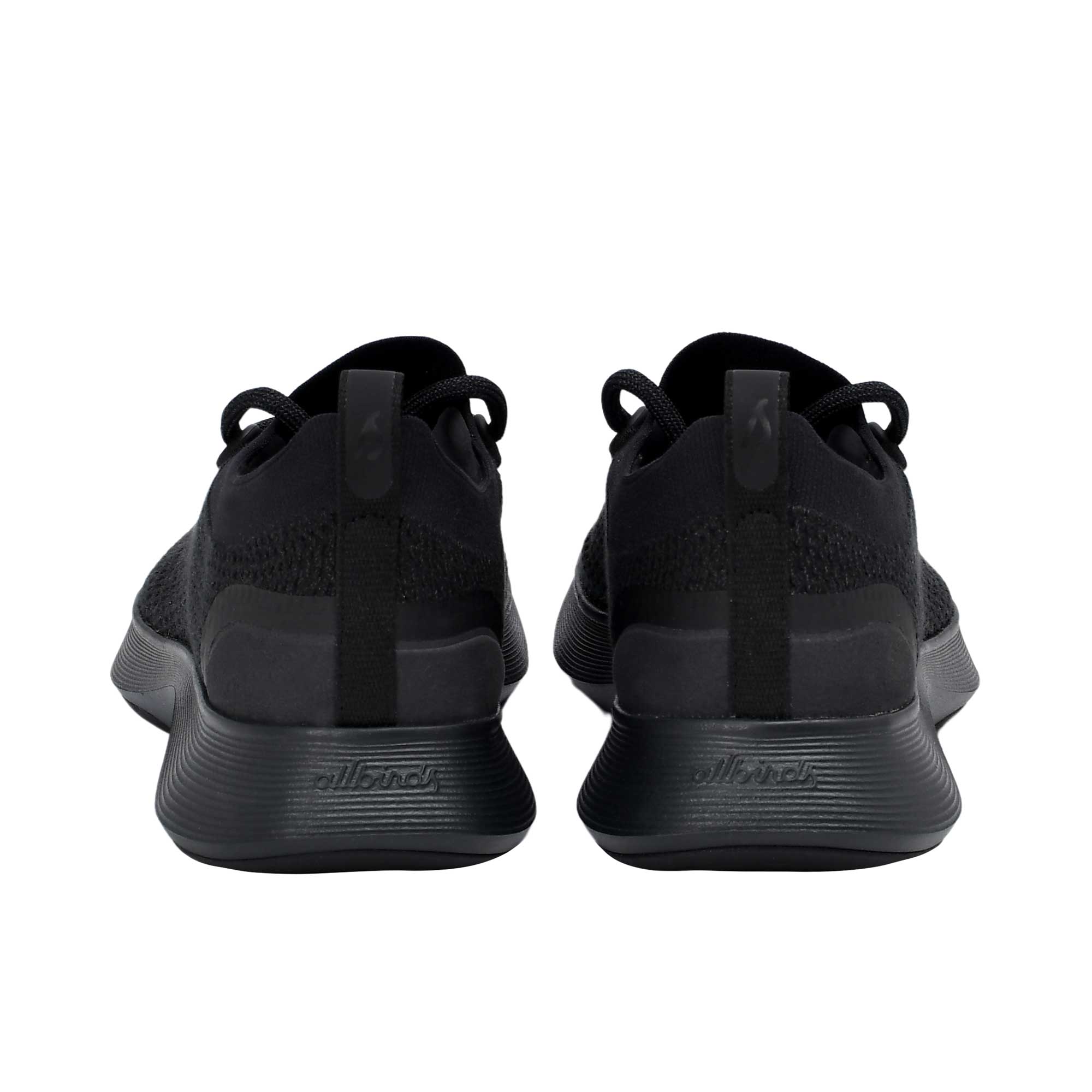 Rear view of a pair of black Allbirds Tree Runner sneakers, featuring fabric heel pull tabs and a subtle embossed "allbirds" logo on the textured black midsoles.