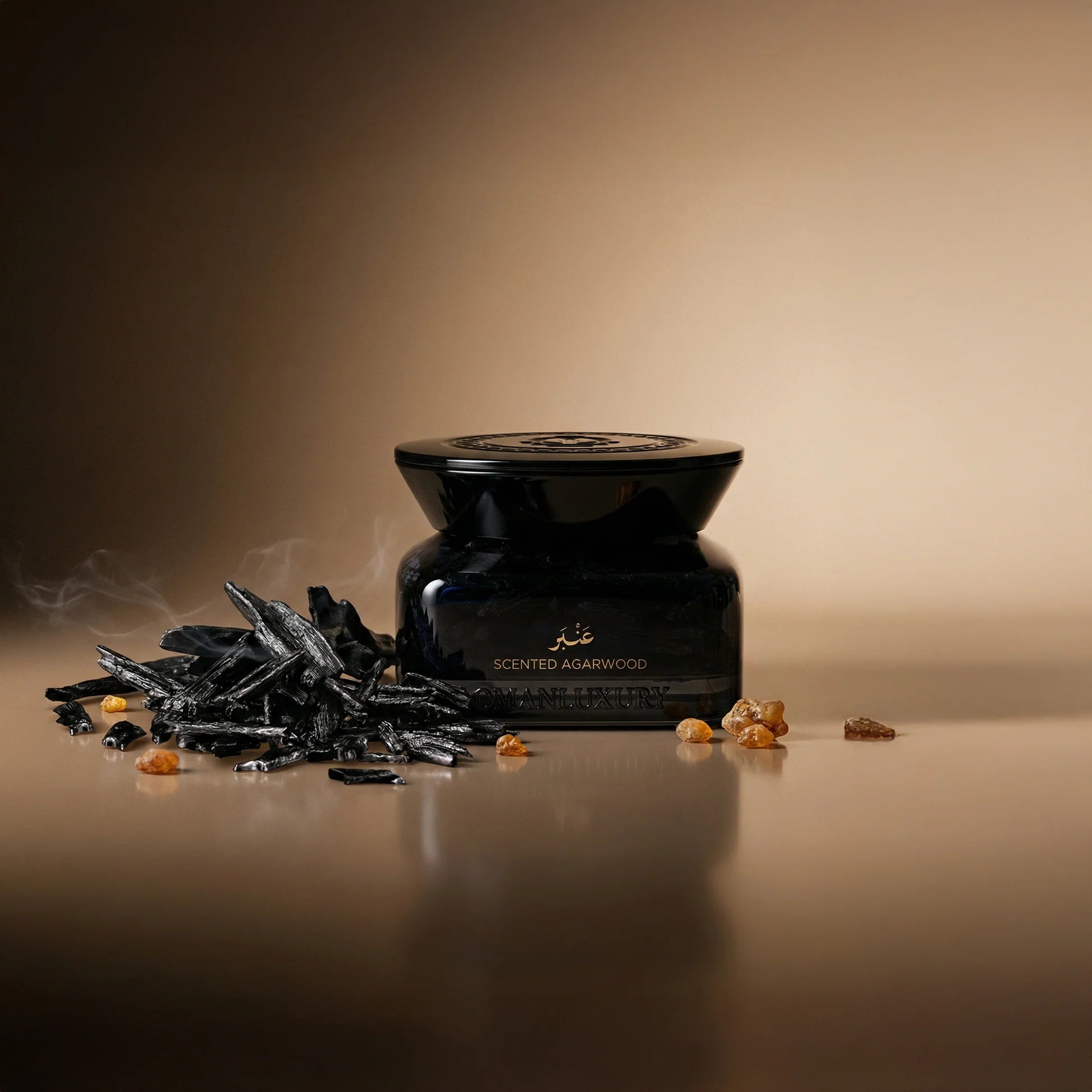 Dark blue jar with gold-toned text and embossed lid, next to a pile of dark agarwood chips and amber resin pieces.
