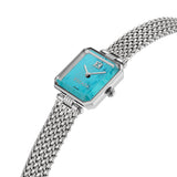 An angled perspective shot of the square silver luxury women's watch, showcasing the beveled stainless steel bezel geometry, the gold-toned crown, and the natural stone textures of the turquoise dial.