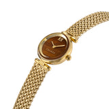 An angled perspective shot of the luxury gold women's watch, showcasing the polished golden bezel, the fluted side crown, and the natural horizontal grain of the brown dial face.