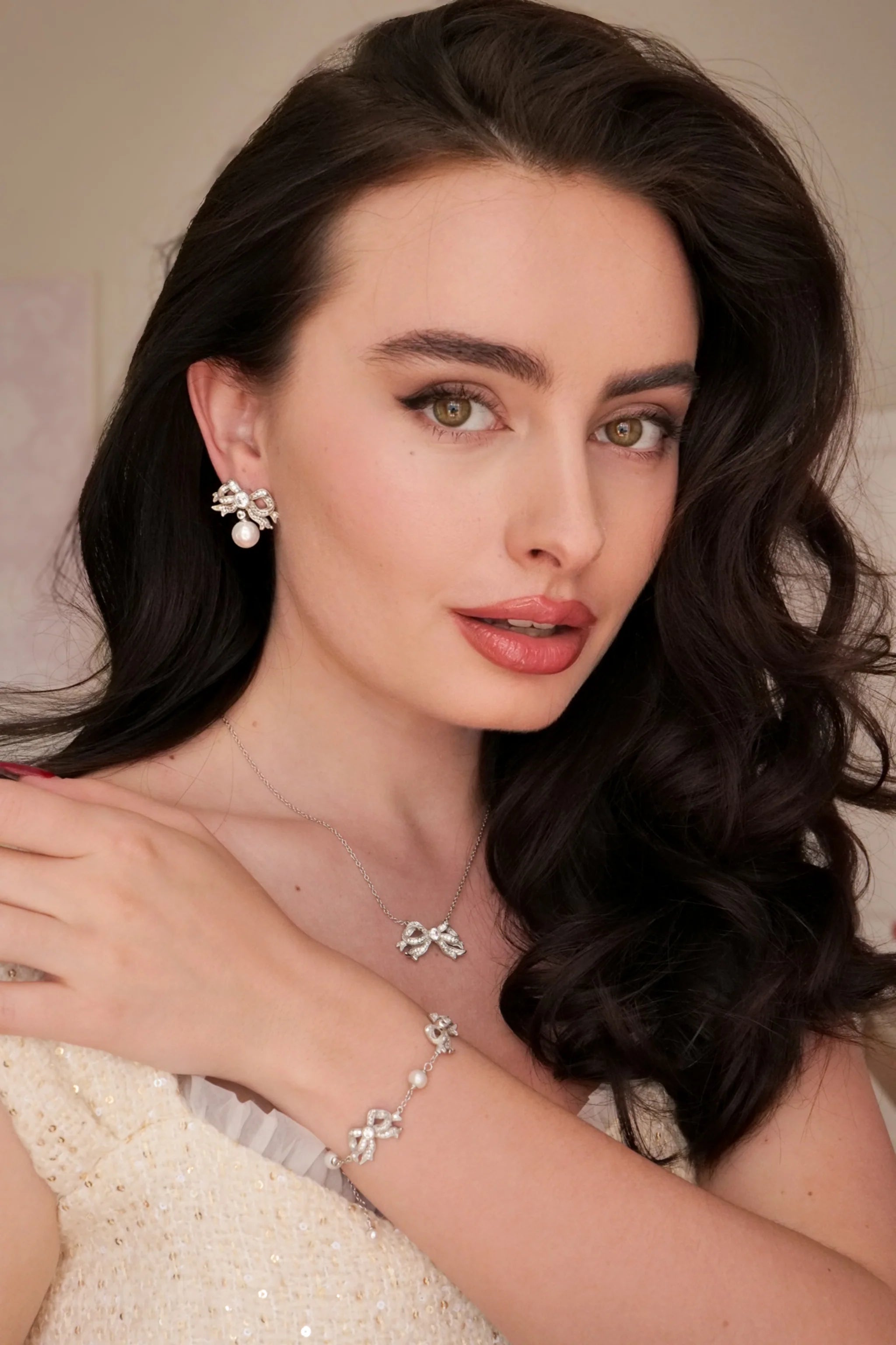 Silver-toned bow earring with clear stones and a round white pearl drop.