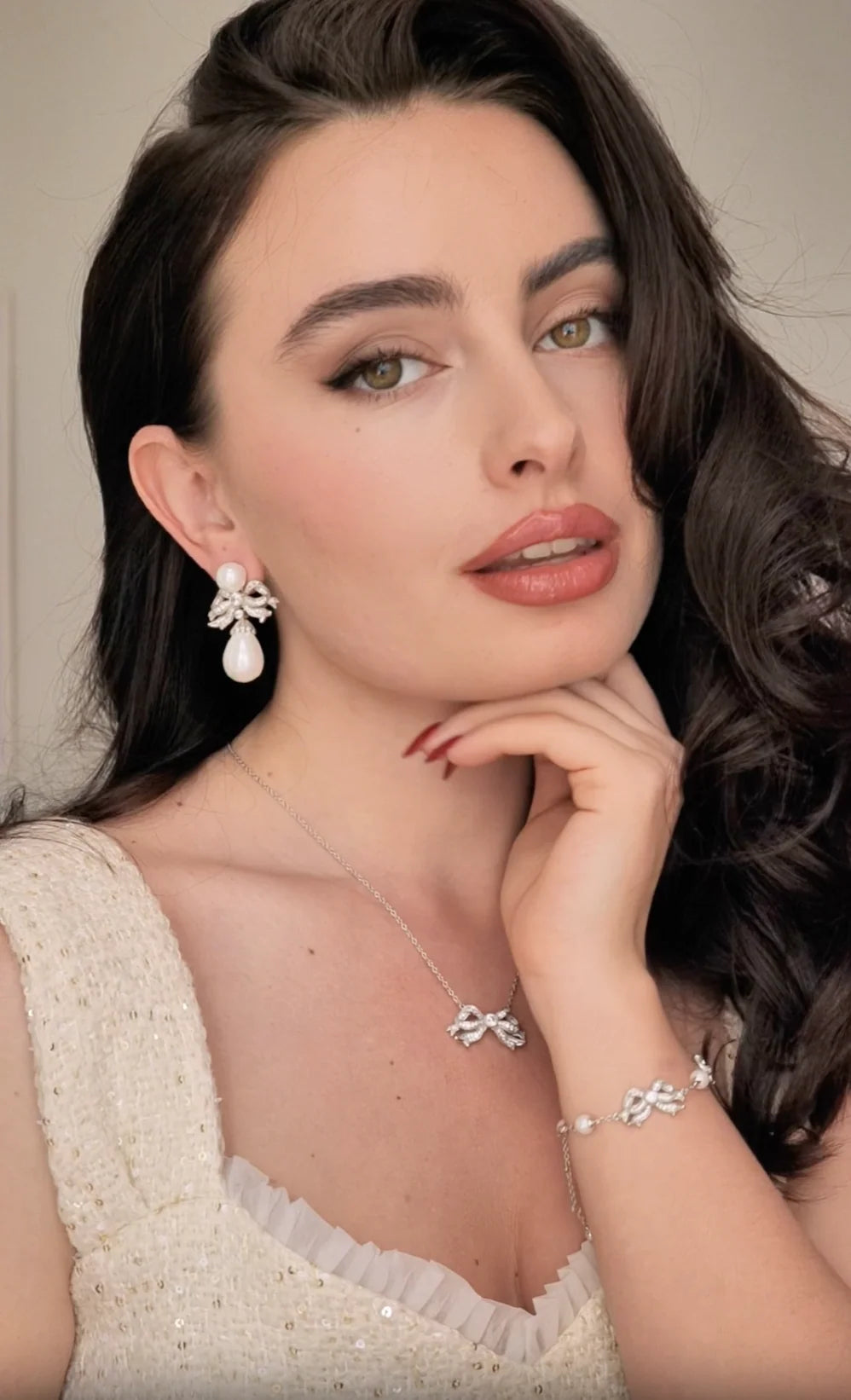 Silver-toned drop earring with a round pearl stud, a sparkling bow, and a dangling tear-drop pearl.