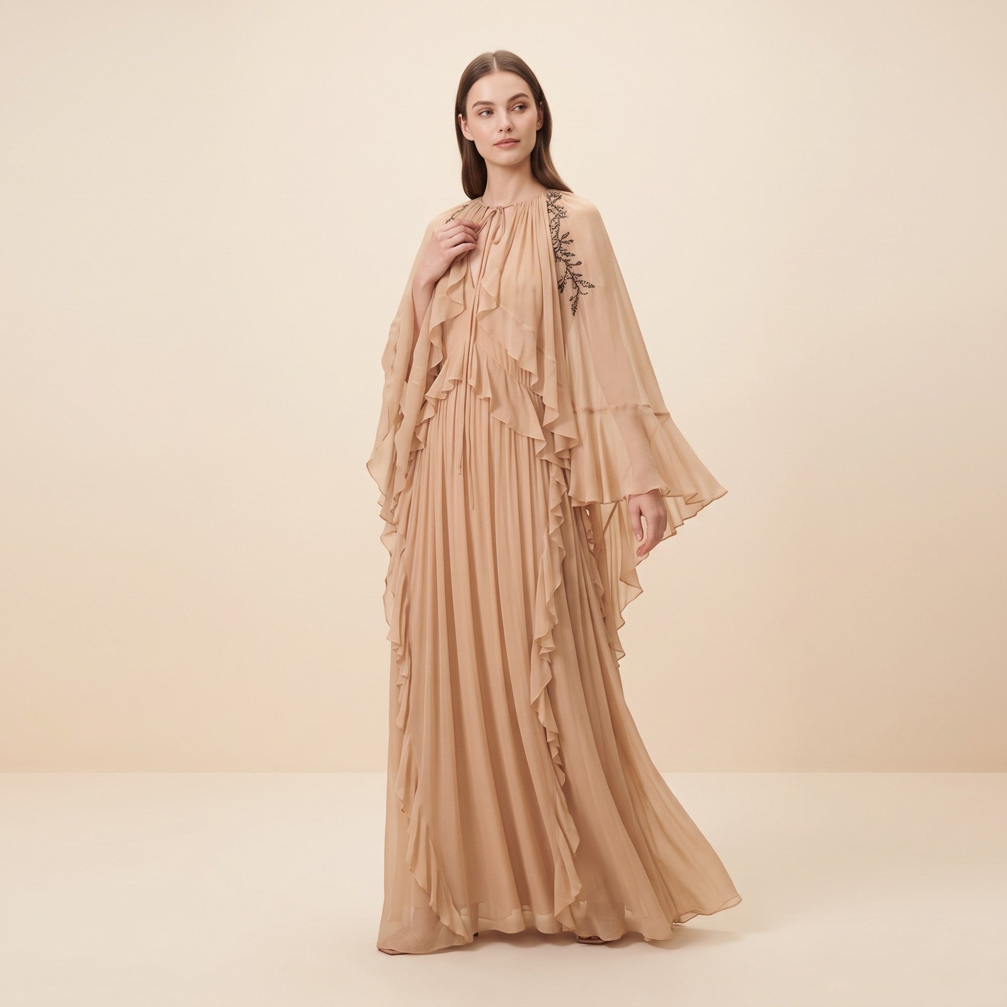 Powder-colored maxi dress with a ruffled bodice, pleated skirt, flowing sleeves, and black beaded floral embroidery on the le