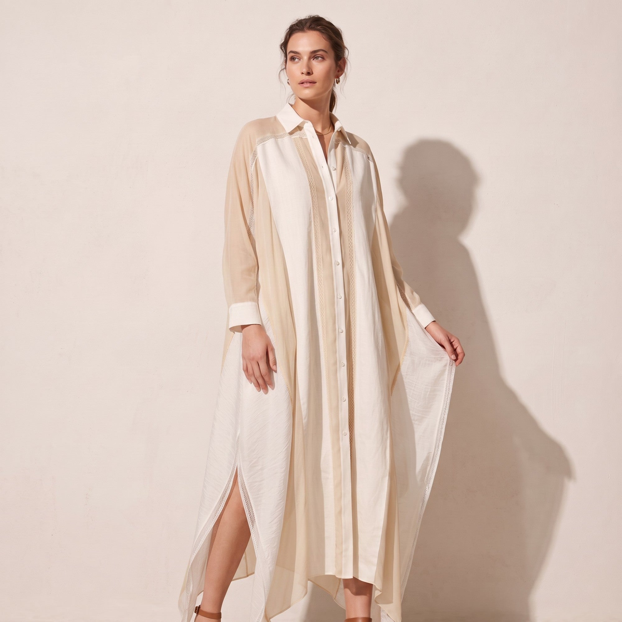 Long beige and off-white panelled shirt dress with a collar, button front, sheer long sleeves, lace trim, and high side slits