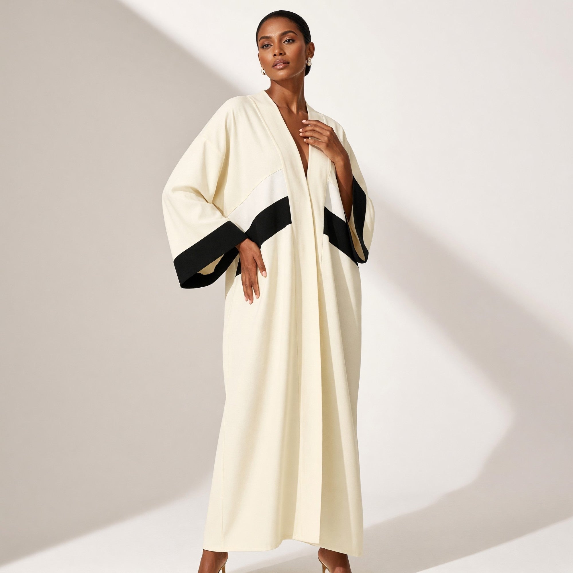 Bone abaya with a V-neck and wide sleeves. Features diagonal black and bone stripes on the front opening and wide black cuffs