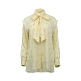 BAQA yellow long-sleeved blouse featuring a geometric polka-dot pattern and a large pussy-bow necktie on a white background.