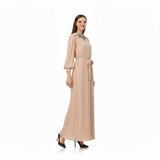 Woman wearing a beige long dress with a belt on a white background.