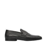 Profile view of a Baldinini black penny loafer showing its detailed woven leather upper, smooth leather saddle strap with a tiny metallic B logo, and a low block-heel rubber sole against a white background.