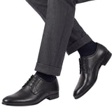 On-model studio shot showcasing the Baldinini black leather Derby shoes being worn with dark grey cuffed trousers and navy blue socks against a white background.