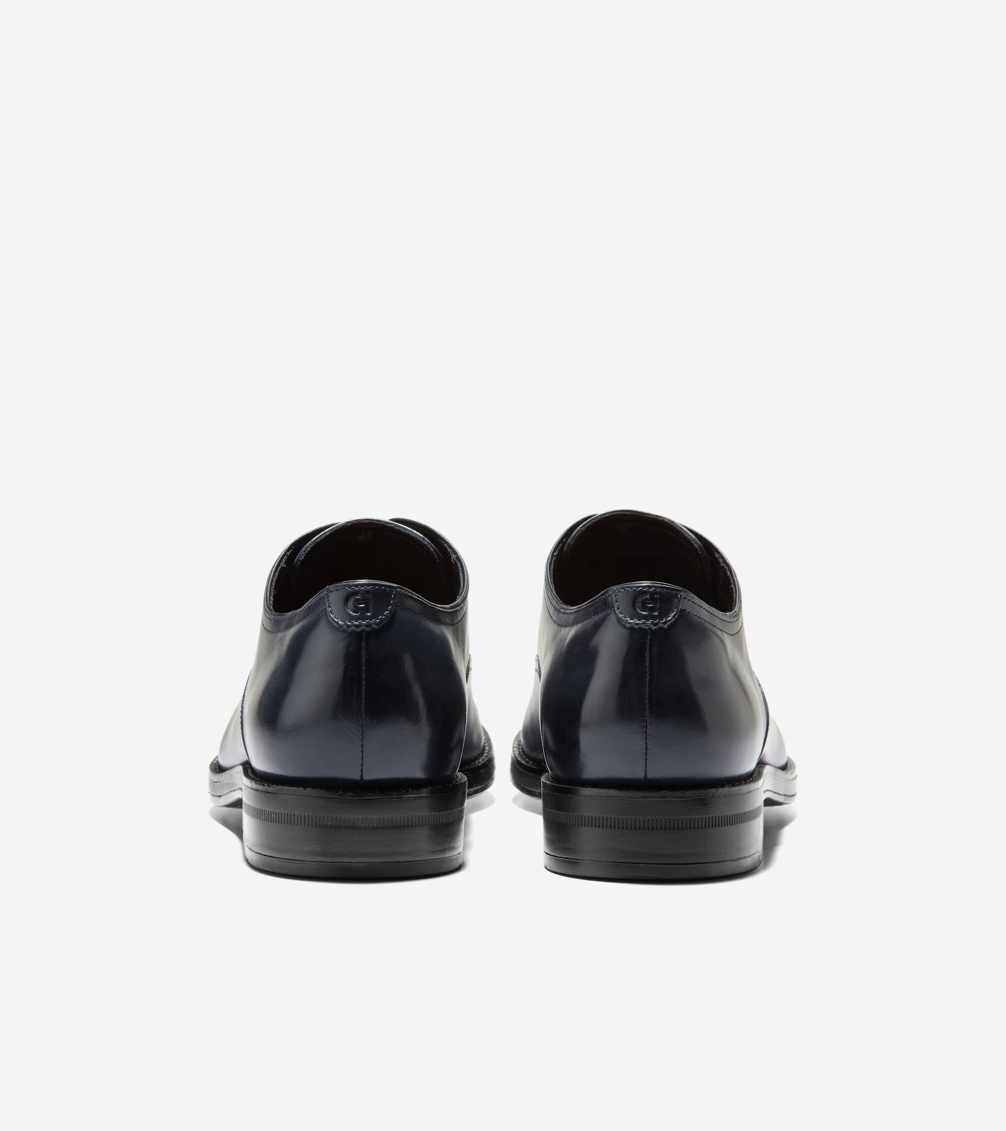 Dark blue polished leather men's oxfords, back view. Each shoe has an embossed 'C' logo on the heel and stacked black heels.