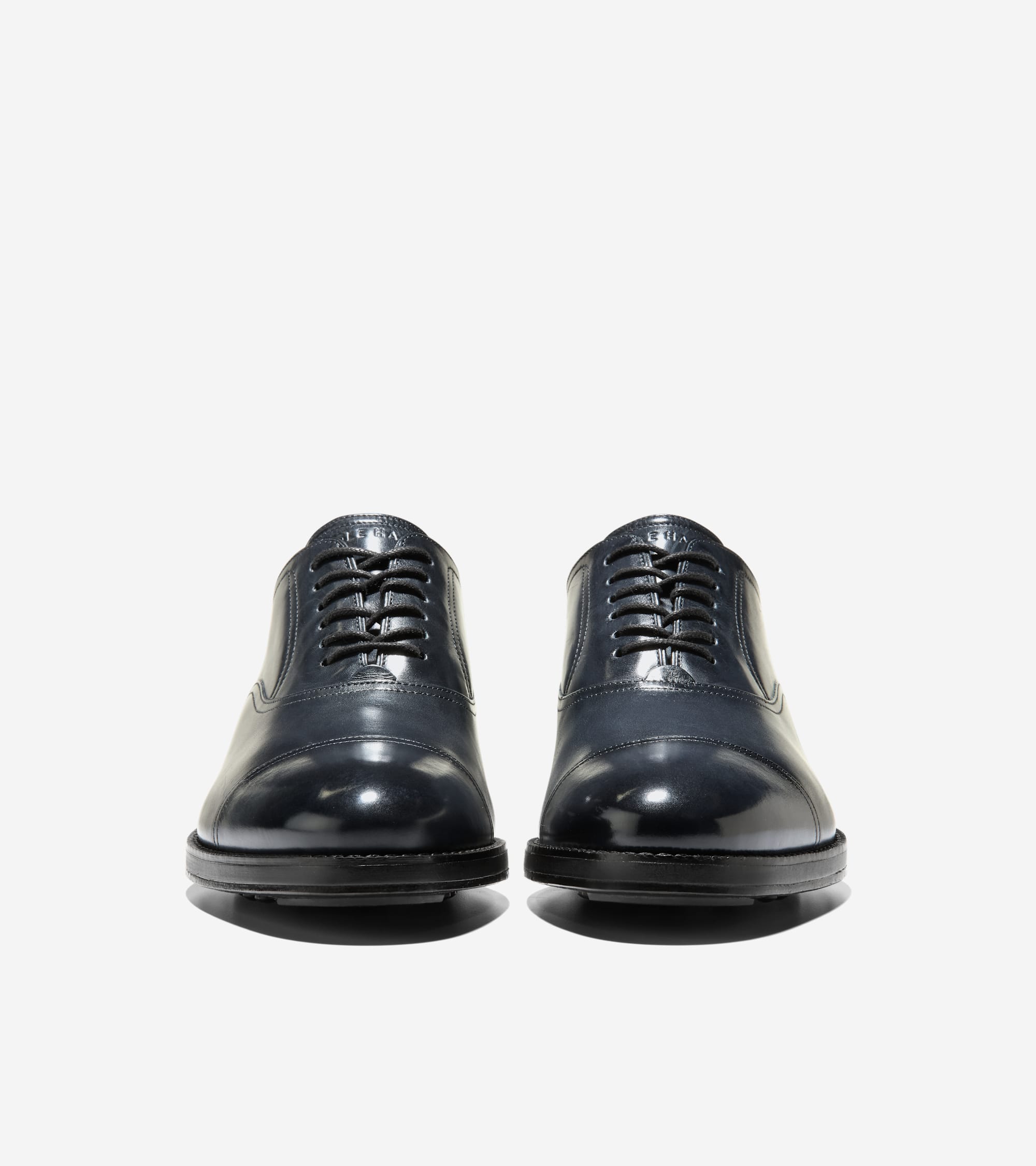 Pair of dark blue polished leather cap toe oxfords with black laces, closed lacing, and black soles.