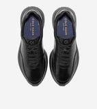A pair of black leather slip-on sneakers with thick black soles and elastic laces. Blue insoles are visible with "COLE HAAN N