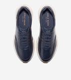 Pair of navy blue leather slip-on sneakers with decorative laces, gold-toned Cole Haan branding on the insole, and thick off-