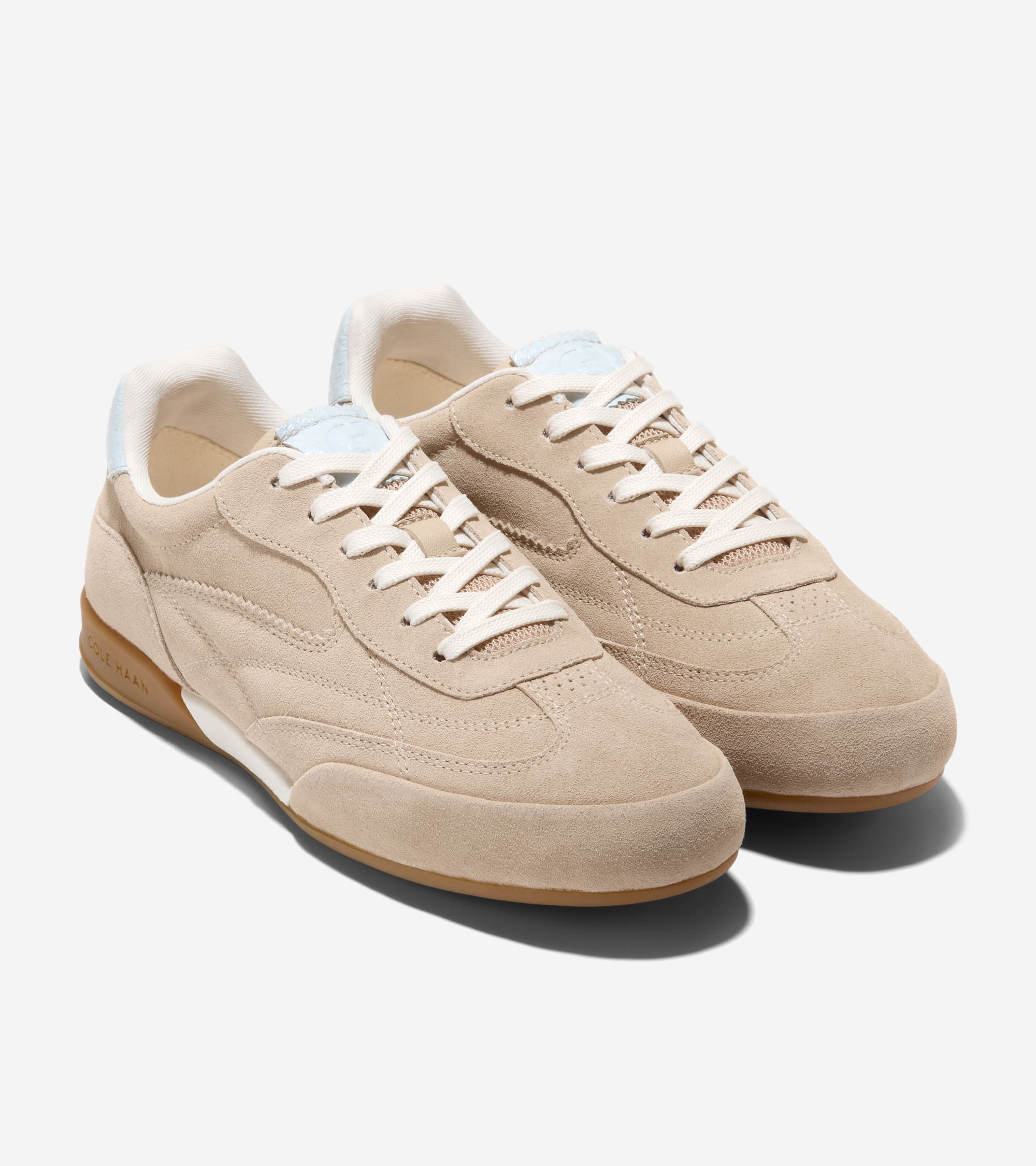 Pair of beige suede low-top sneakers with white laces, light blue tongue labels, white midsole stripe, and brown gum soles.