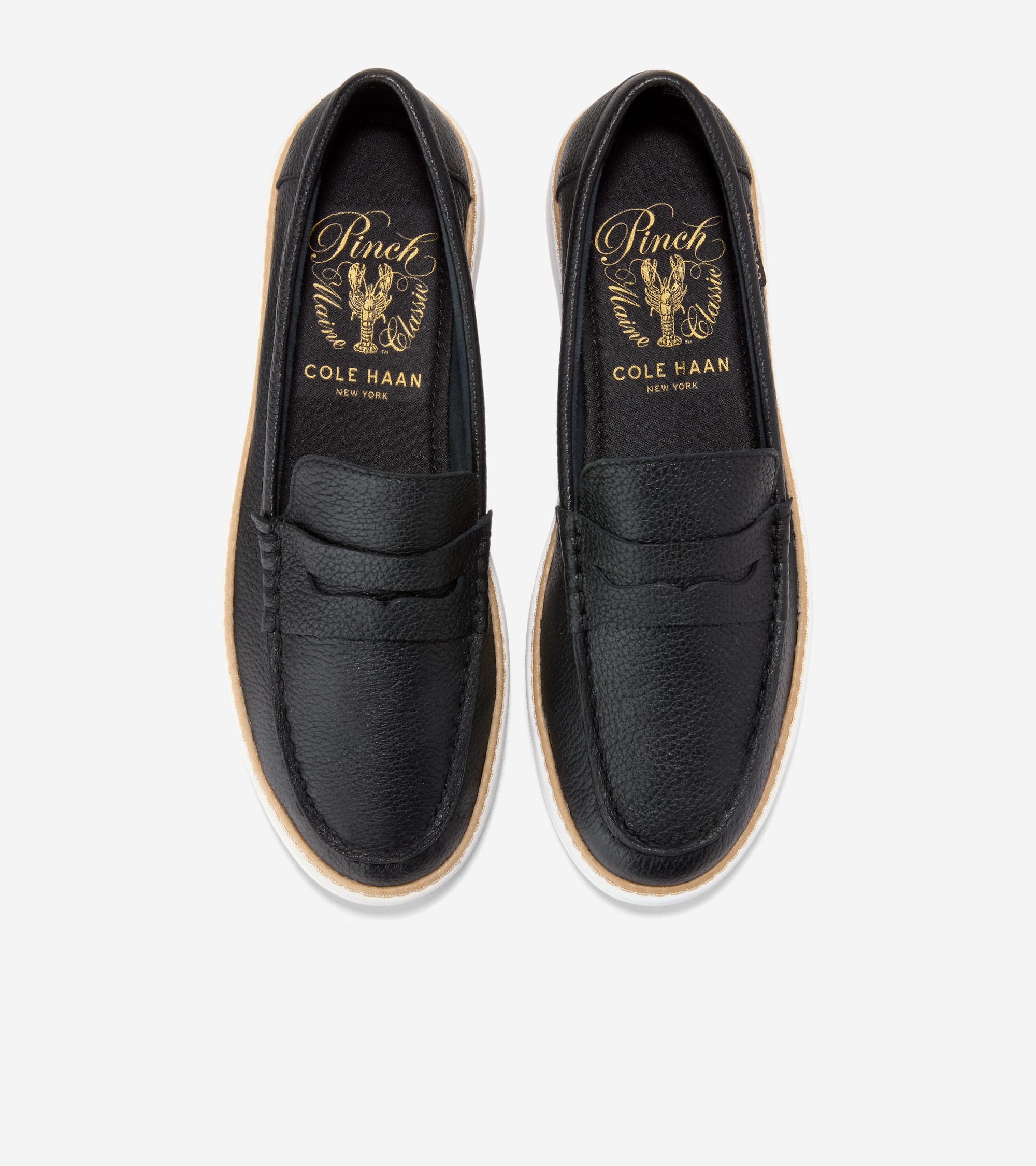Pair of black pebbled leather penny loafers with white soles and tan trim. Gold-toned Cole Haan logo inside.