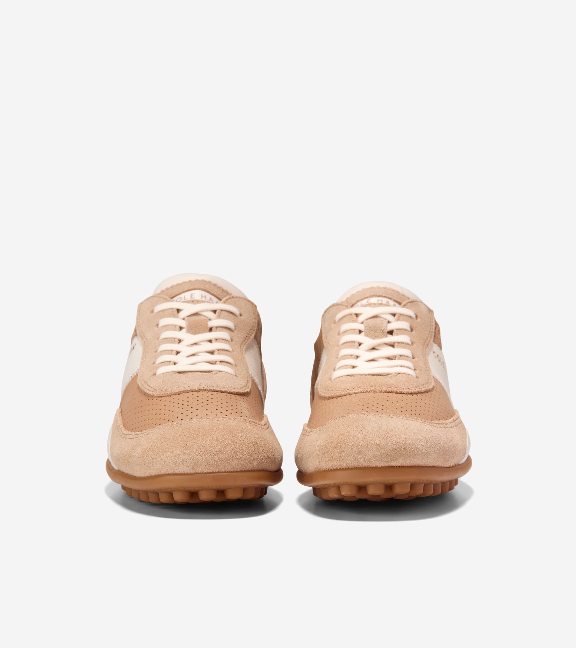 Pair of tan suede and cream sneakers with perforated toe boxes, white laces, and brown rubber soles with nubs.