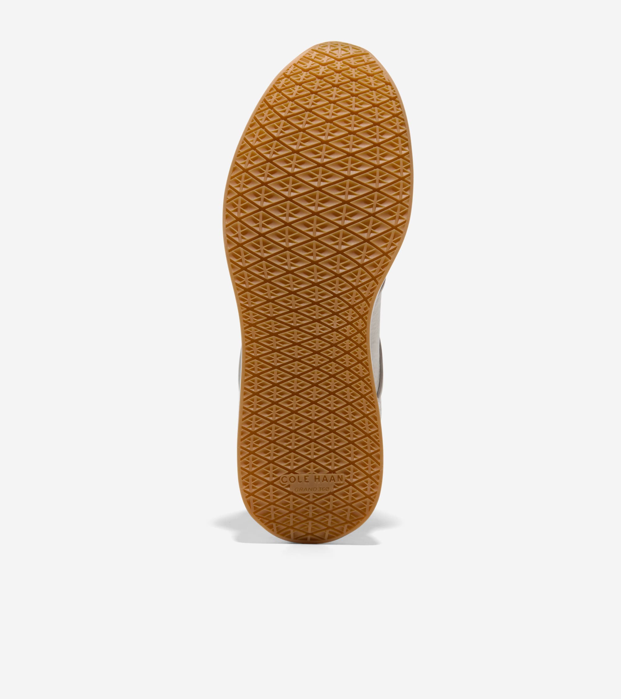 Bottom view of a sneaker with a brown gum sole featuring a diamond-patterned tread and "COLE HAAN GRAND.TØS" embossed on the