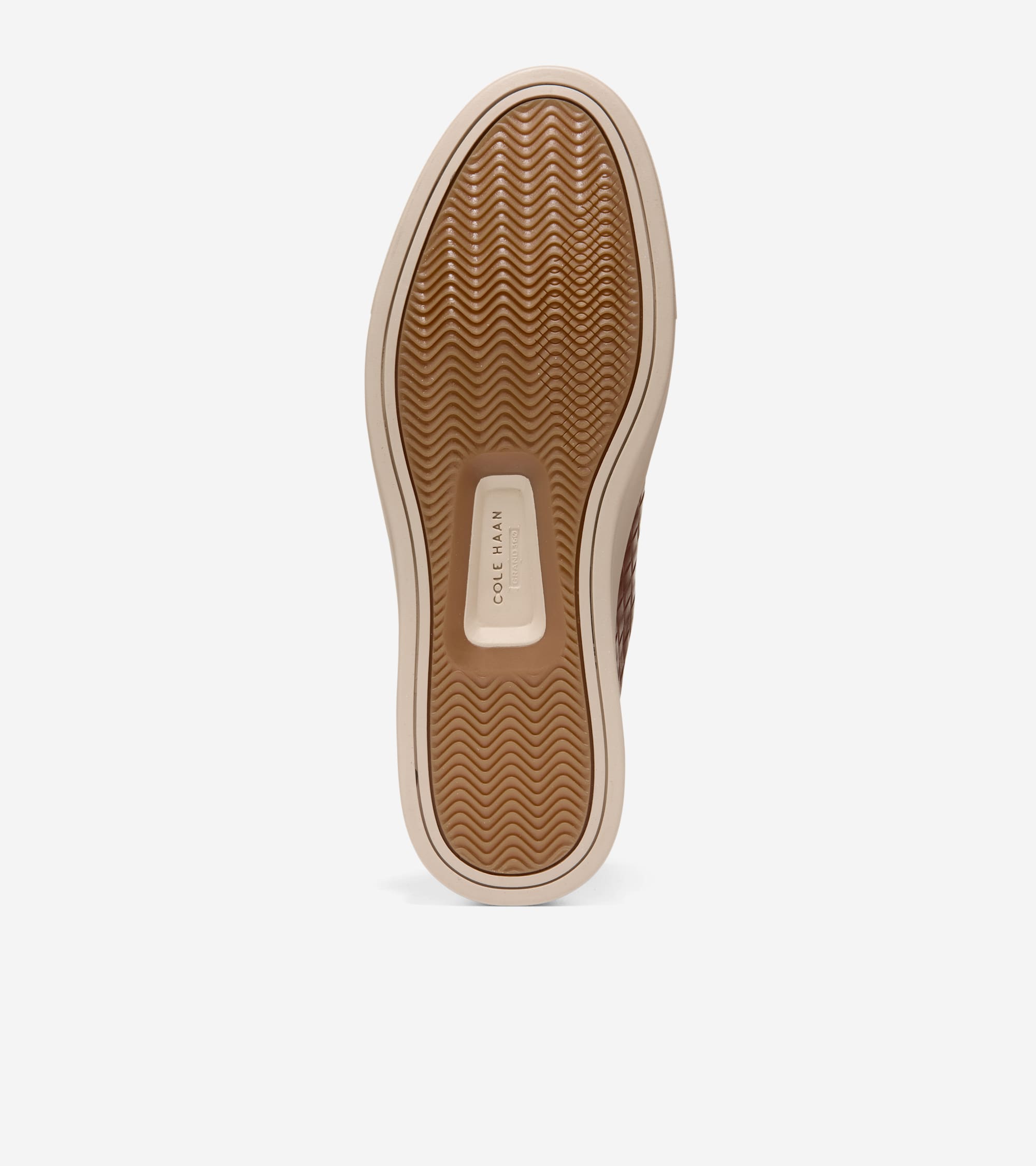 Brown rubber sole of a sneaker with a wavy traction pattern, cream trim, and Cole Haan GrandPrø branding.