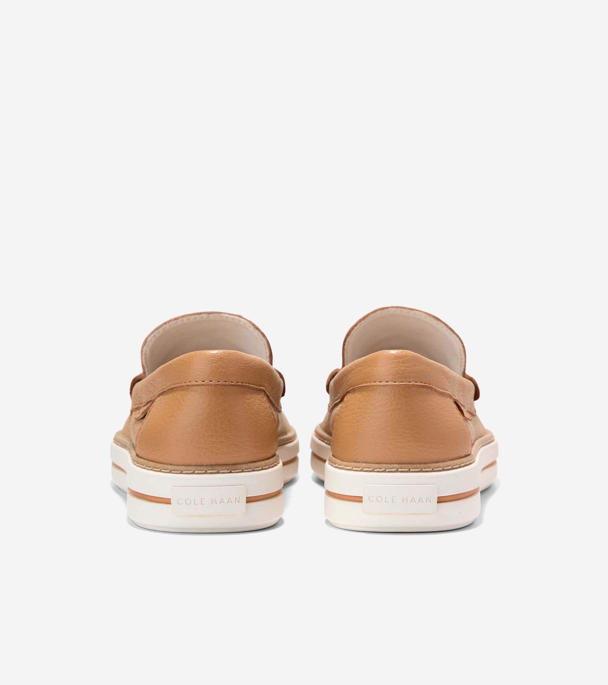 Tan textured leather penny loafers with thick white platform soles, a tan stripe, and 'COLE HAAN' on the heel.