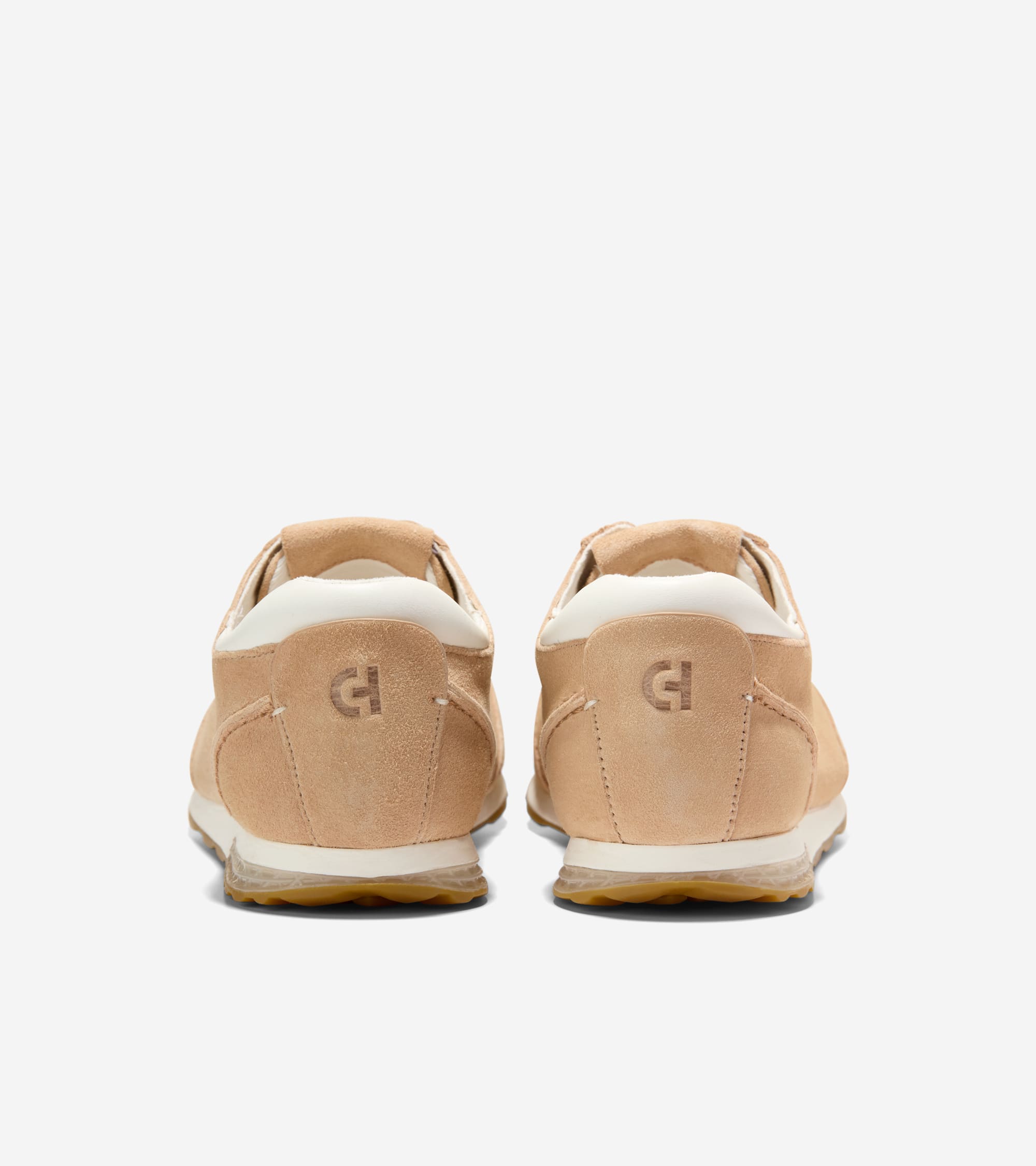 Two light tan suede sneakers, back view. White trim around the ankle, white midsole, translucent outsole, and an embossed log